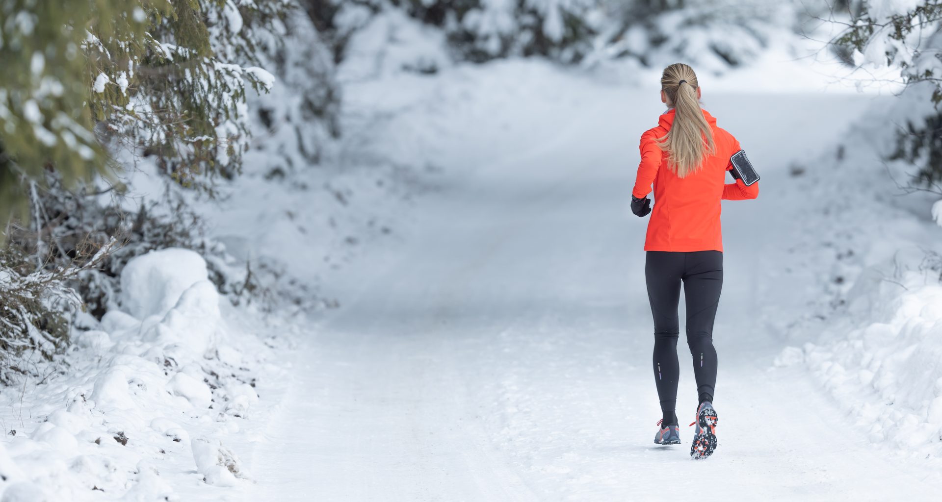 Runner in orange jacket on a snowy forest path, seen from behind.