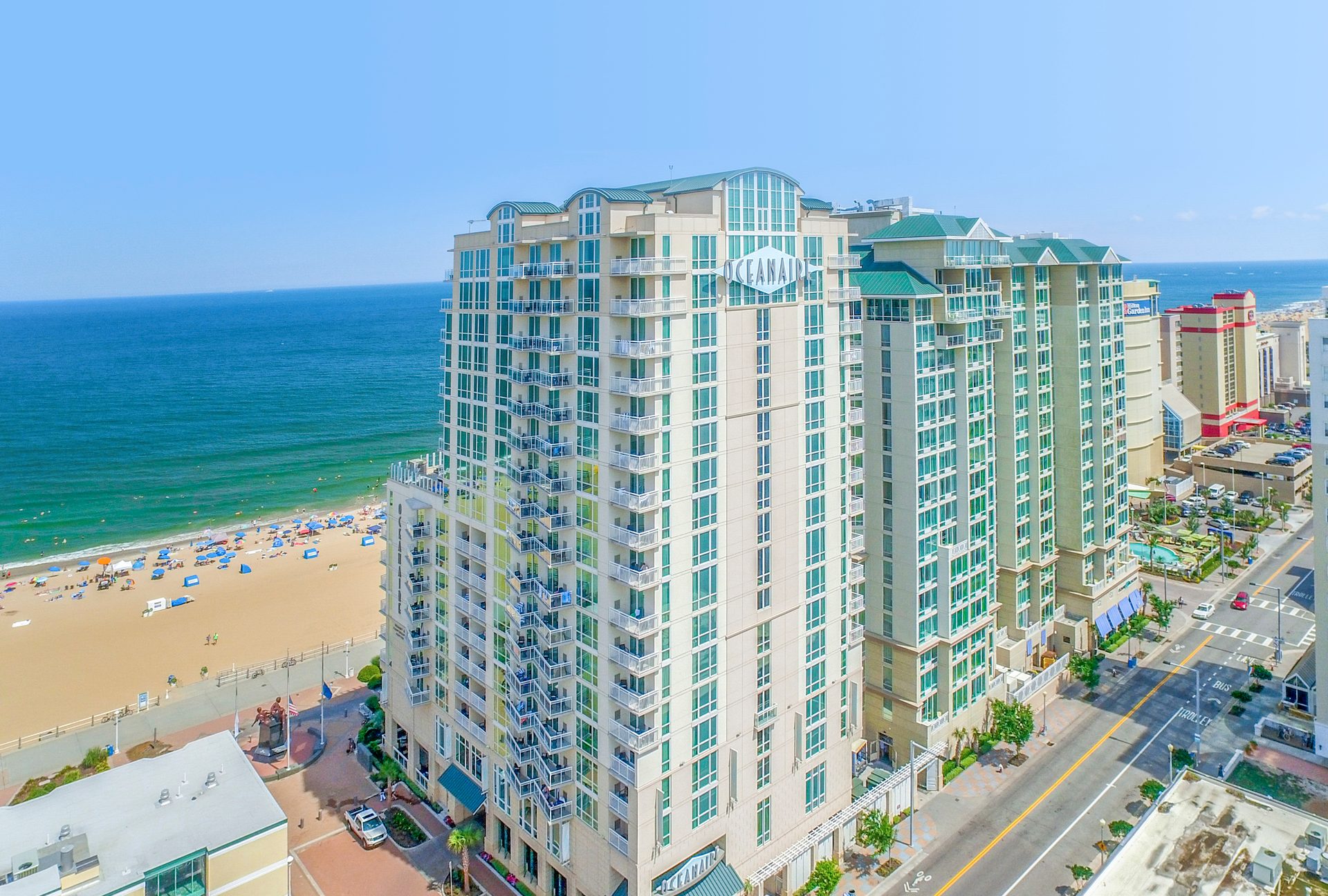 Aerial view of a large beachfront resort building named "OCEANAIR" next to a sandy beach and ocean.