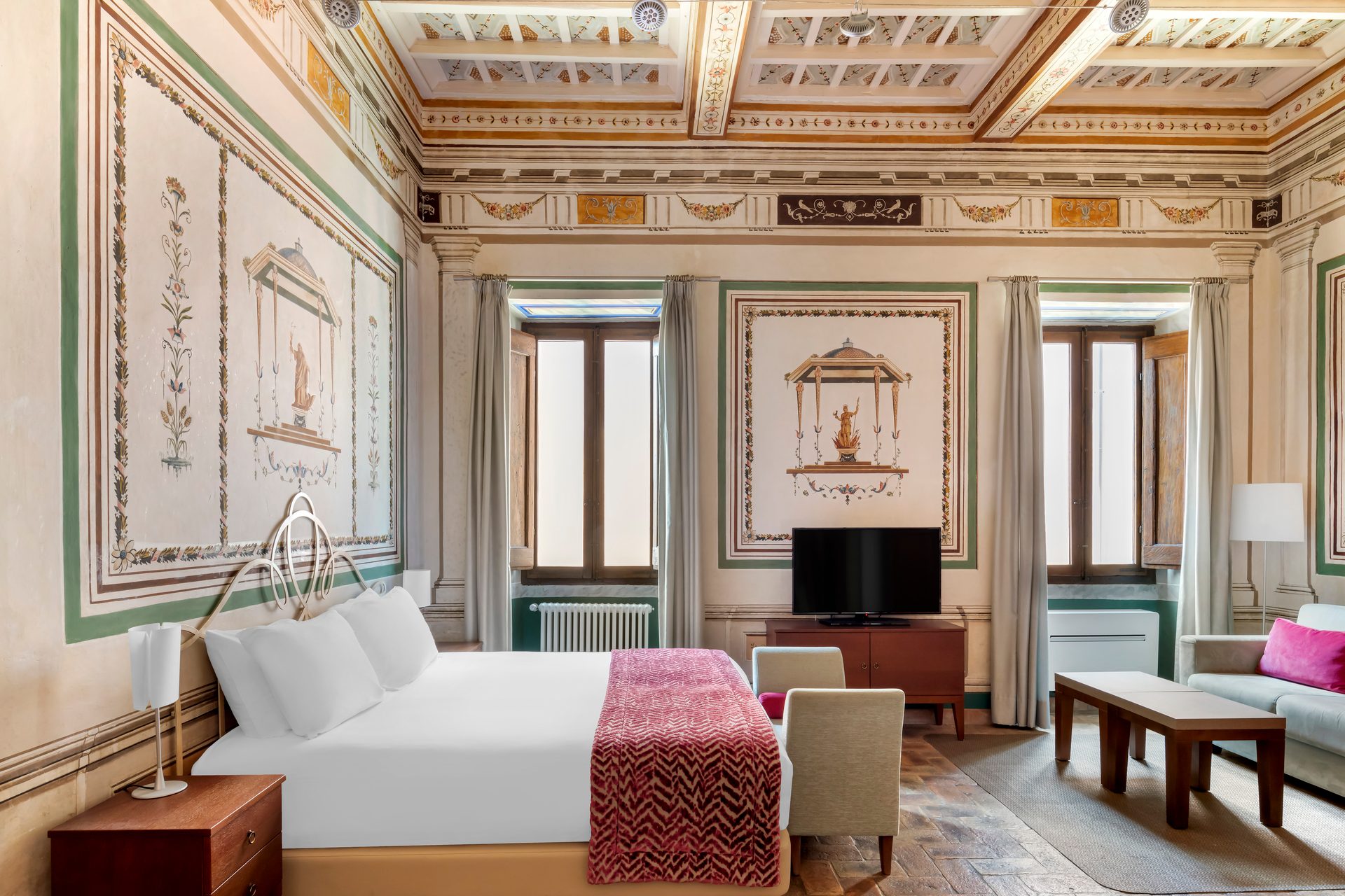 Lavish bedroom with classical frescoes on walls and ceiling, bed, windows, TV, and seating area.