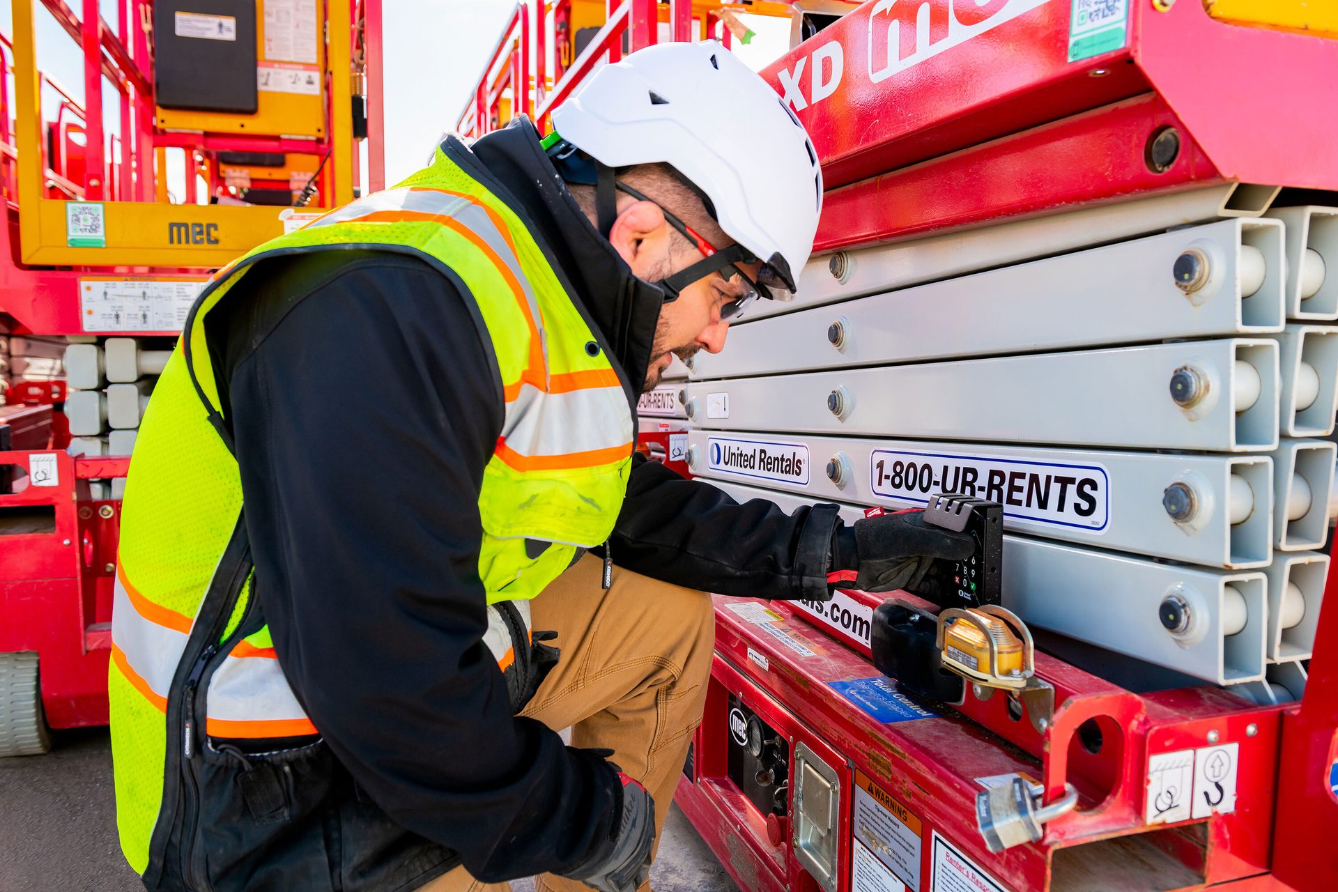 Worker in safety gear operating controls on a United Rentals scissor lift.