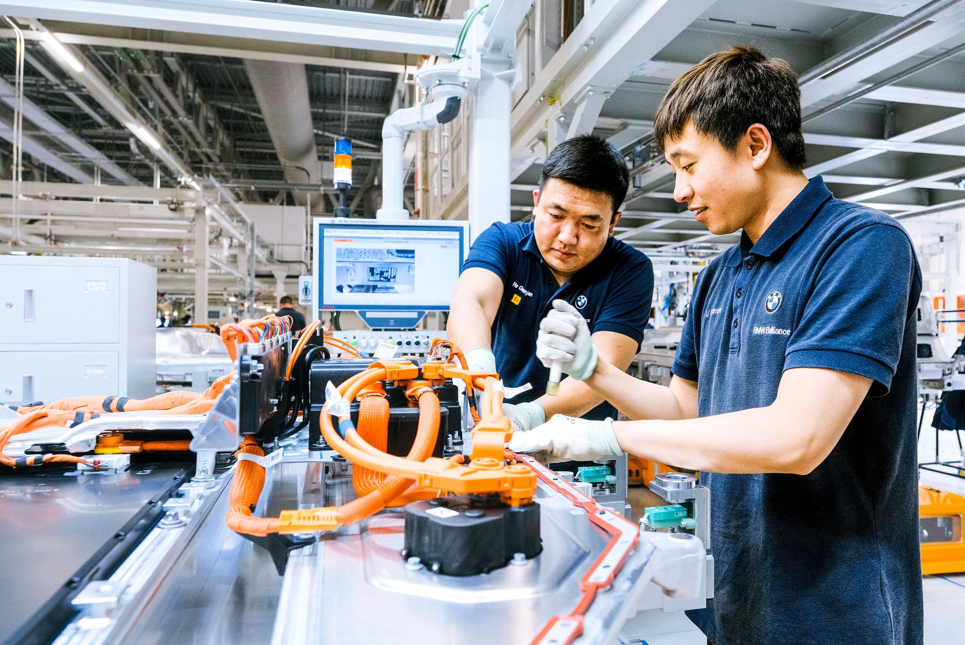 BMW workers assemble orange-cabled machinery in a factory.