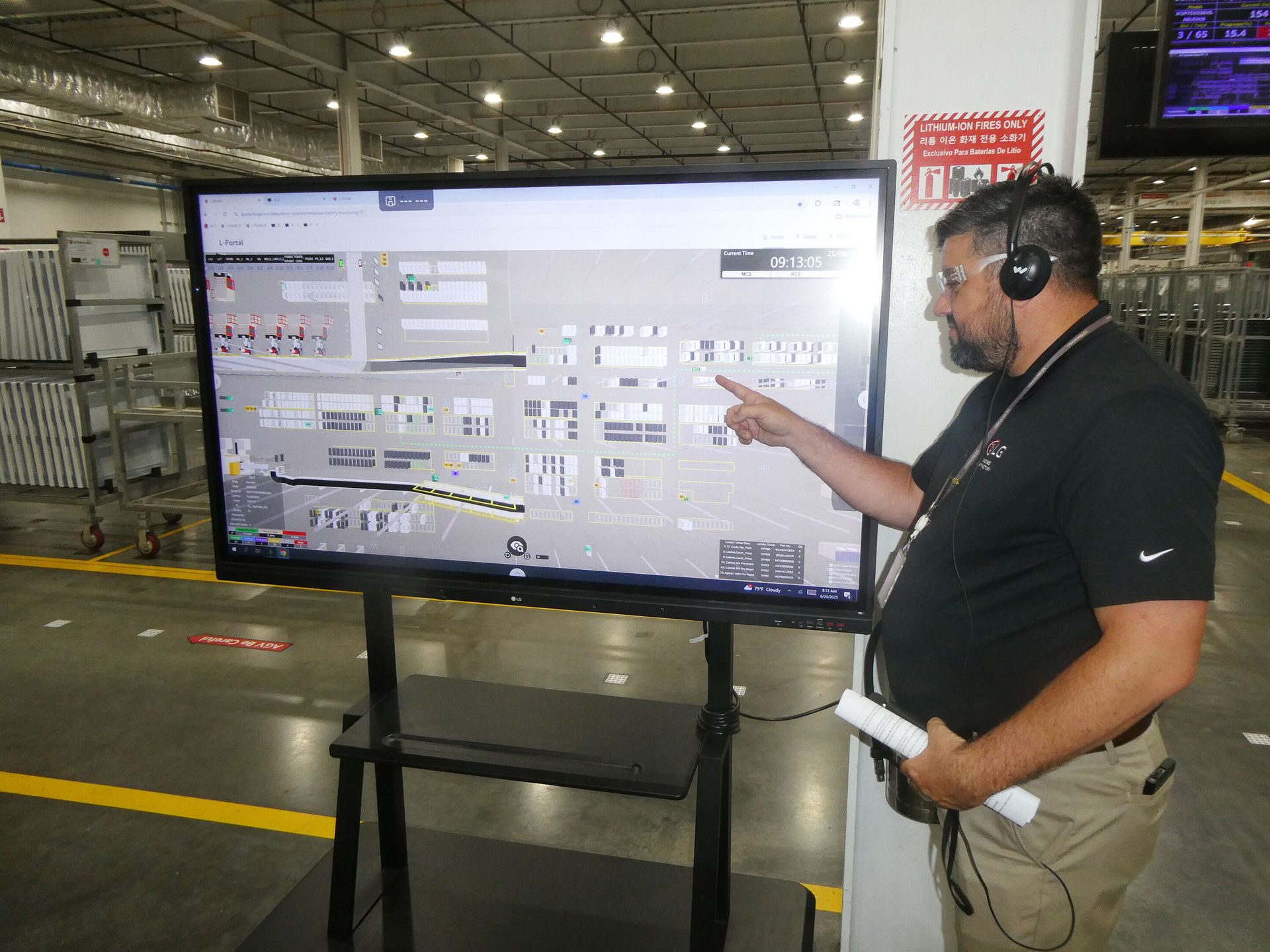 Man points at large factory monitoring screen. Lithium-ion fire warning sign prominent.