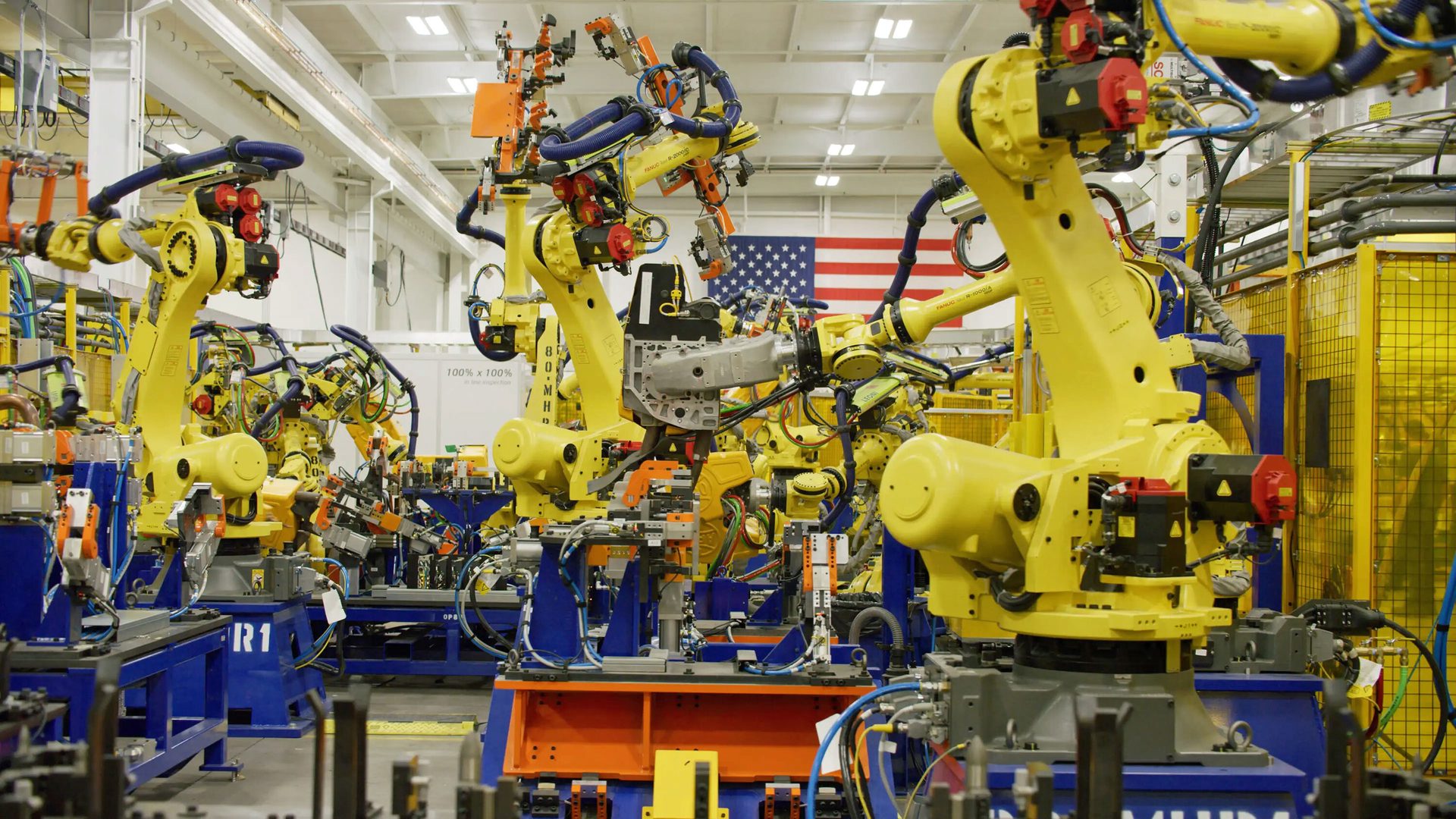 A factory production line with many yellow industrial robots and an American flag.