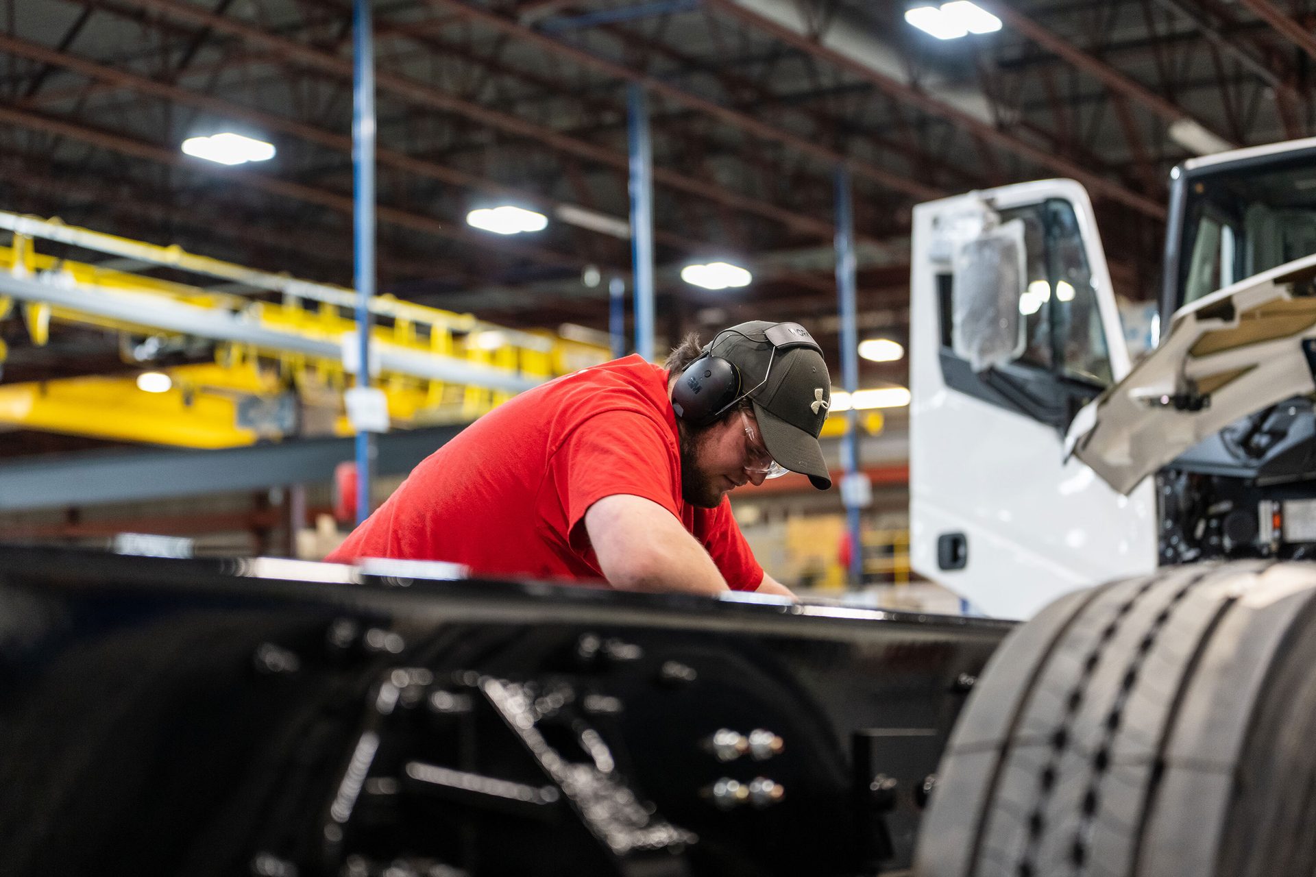 Factory worker in safety gear assembling truck frame.