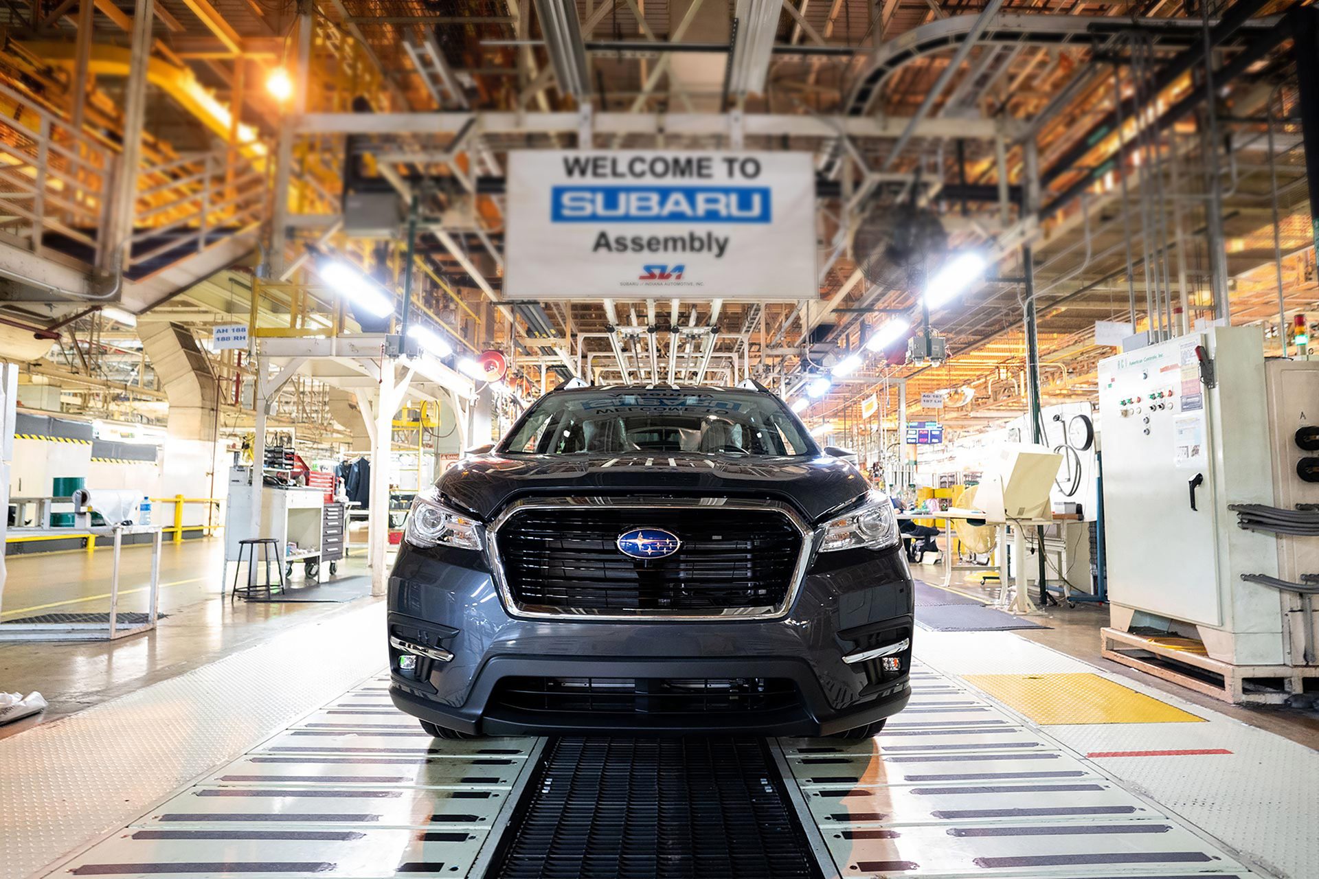 A new dark gray Subaru Ascent SUV on an assembly line with a "WELCOME TO SUBARU Assembly" sign above.