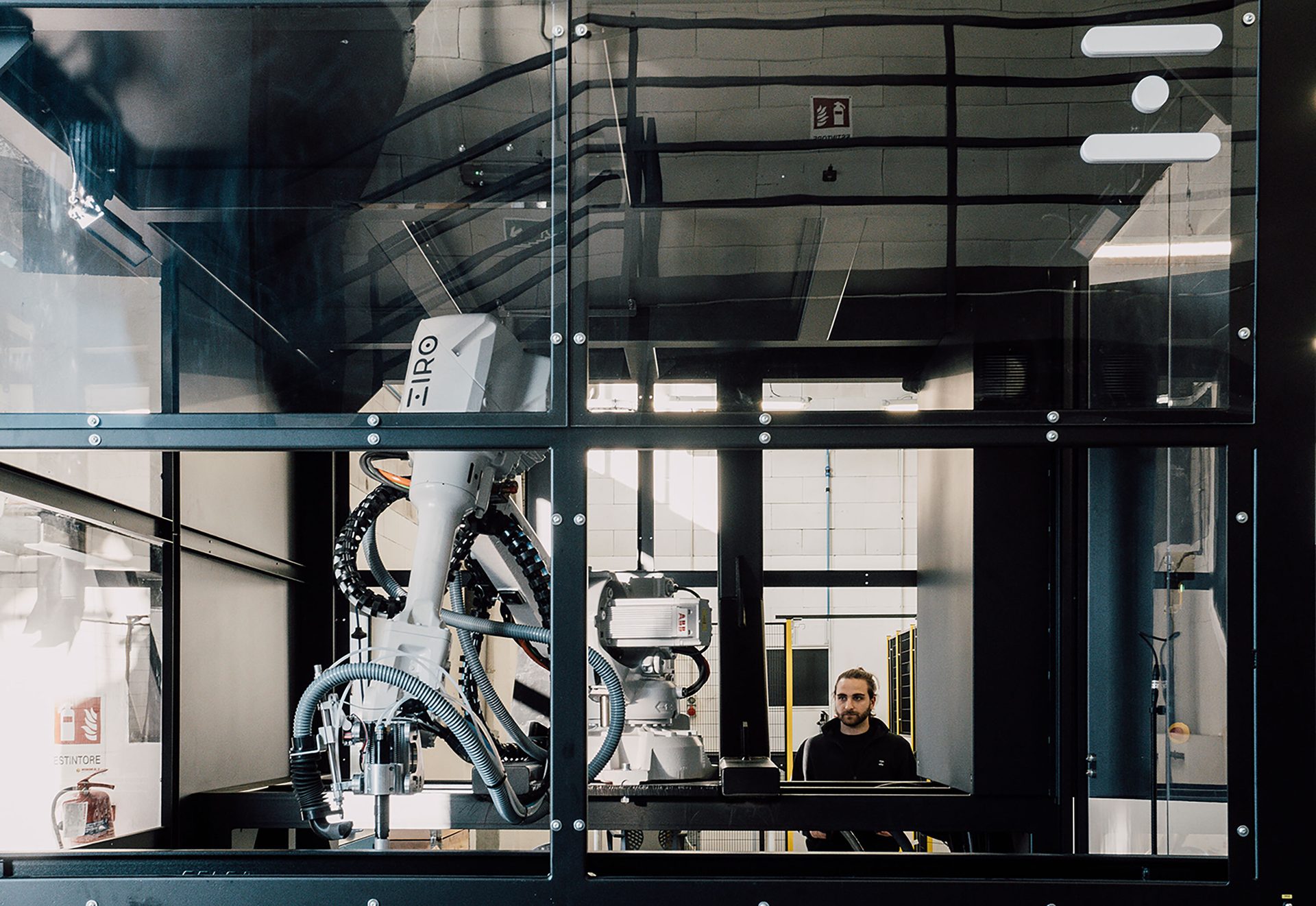 Man observing a robotic arm in a glass-enclosed industrial machine.