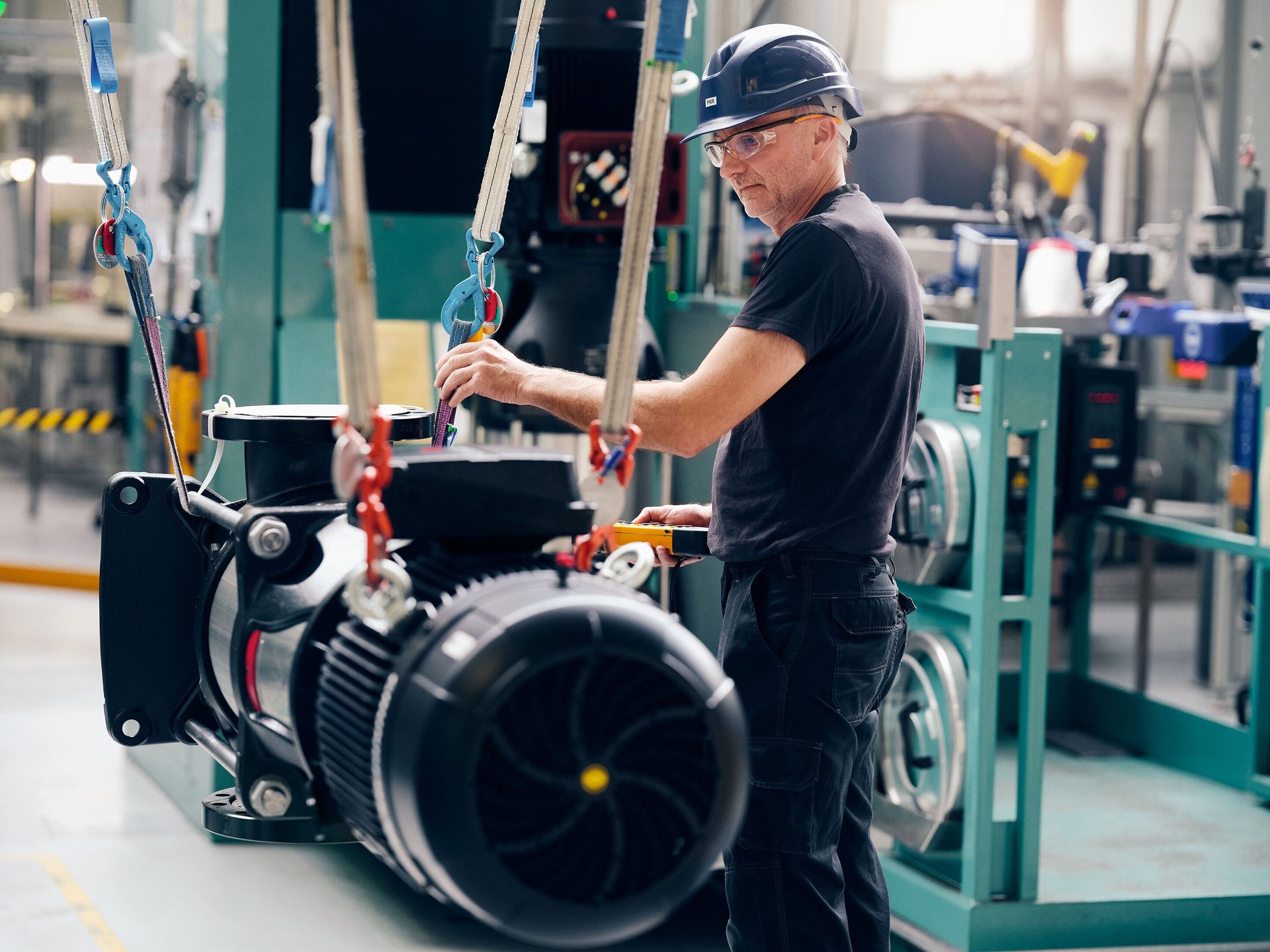 Worker hoists industrial pump in factory with remote control.