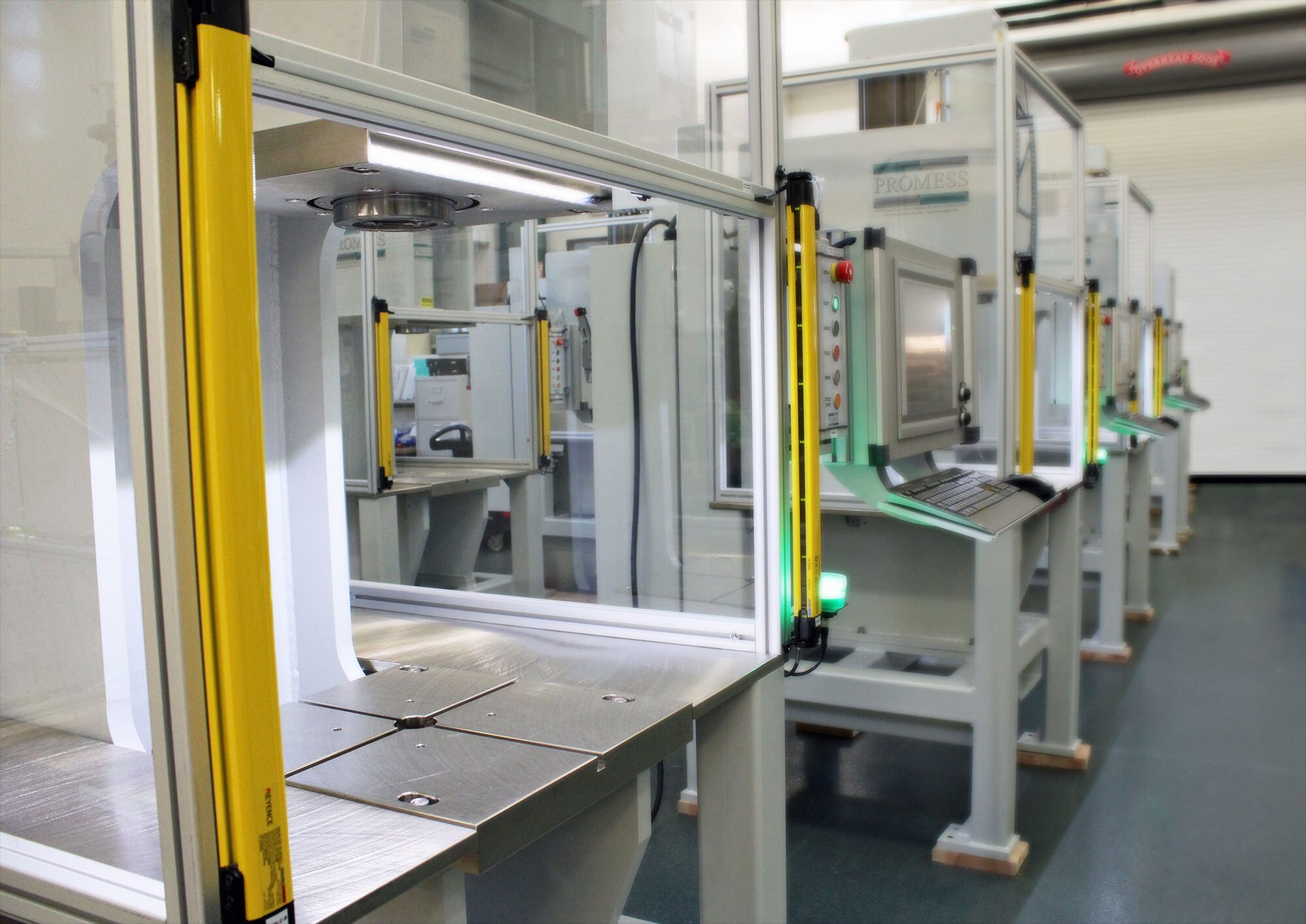 Row of industrial machines with safety light curtains and clear guards in a manufacturing facility.