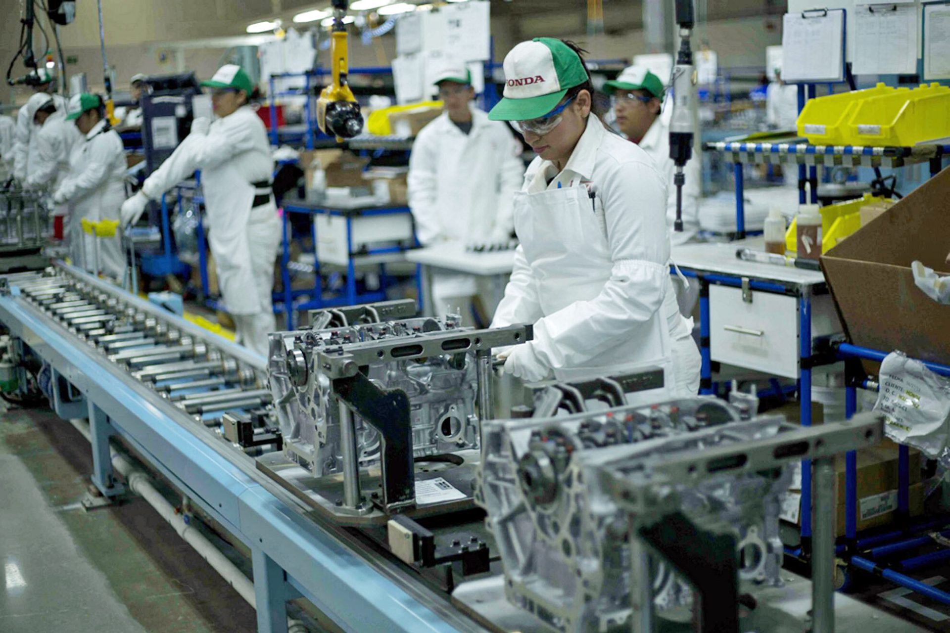 Workers in a Honda factory assembling engine parts on an assembly line.