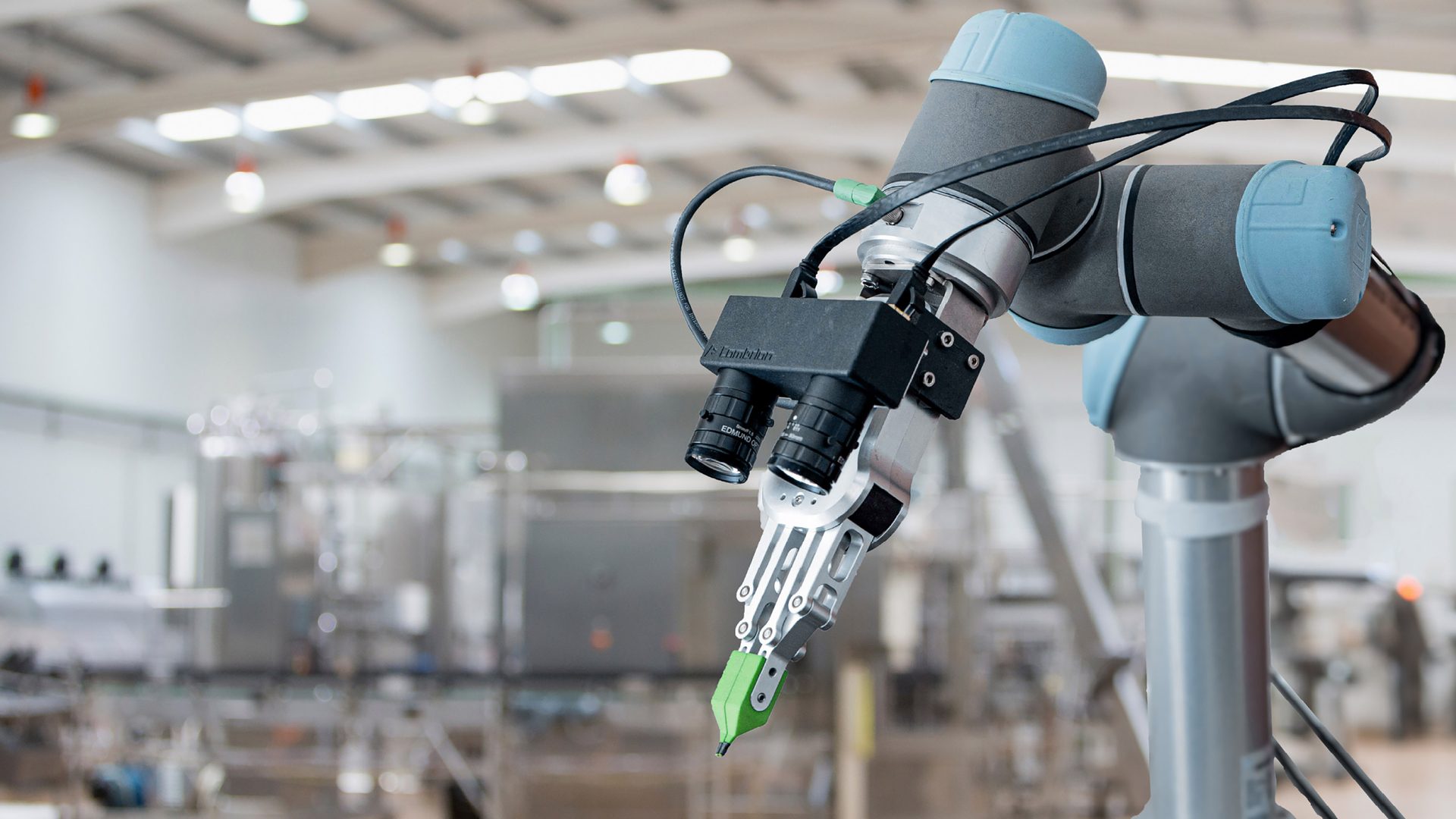Robotic arm with vision system and gripper working in a manufacturing facility.