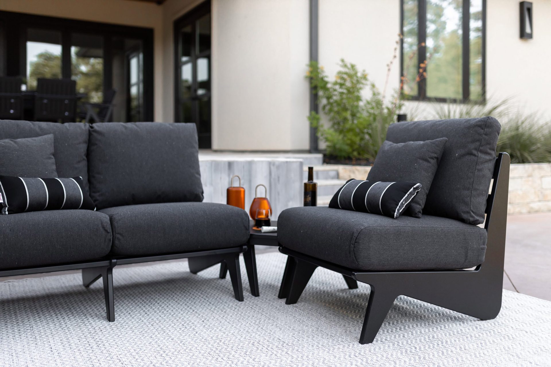 Modern dark gray outdoor sofa and armchair with striped pillows on a light rug.