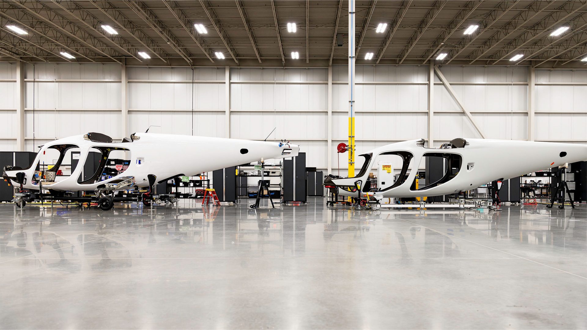 Two white aircraft fuselages being assembled in a bright hangar.