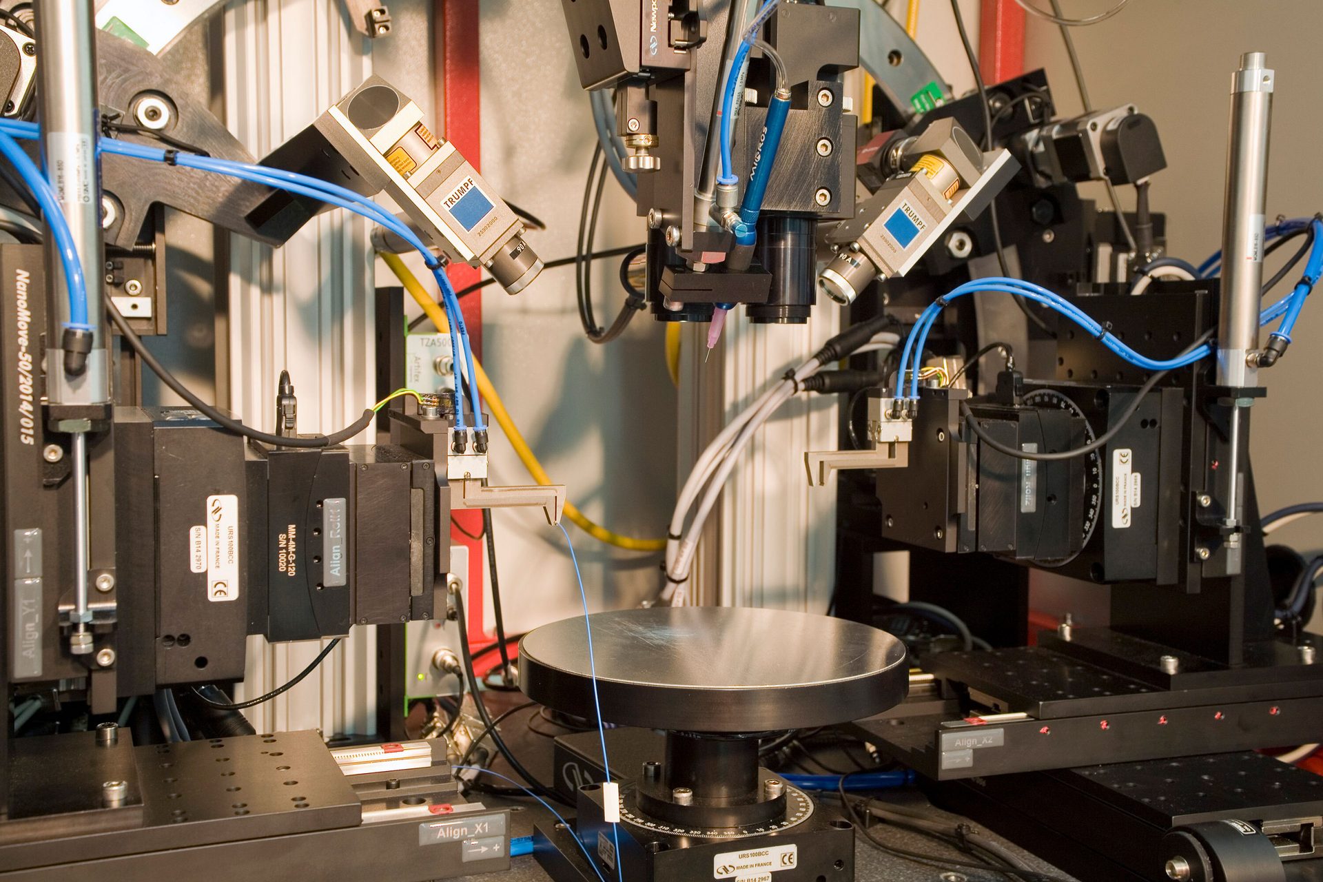 Precision optical alignment and probing system with robotic arms and a central rotating stage.