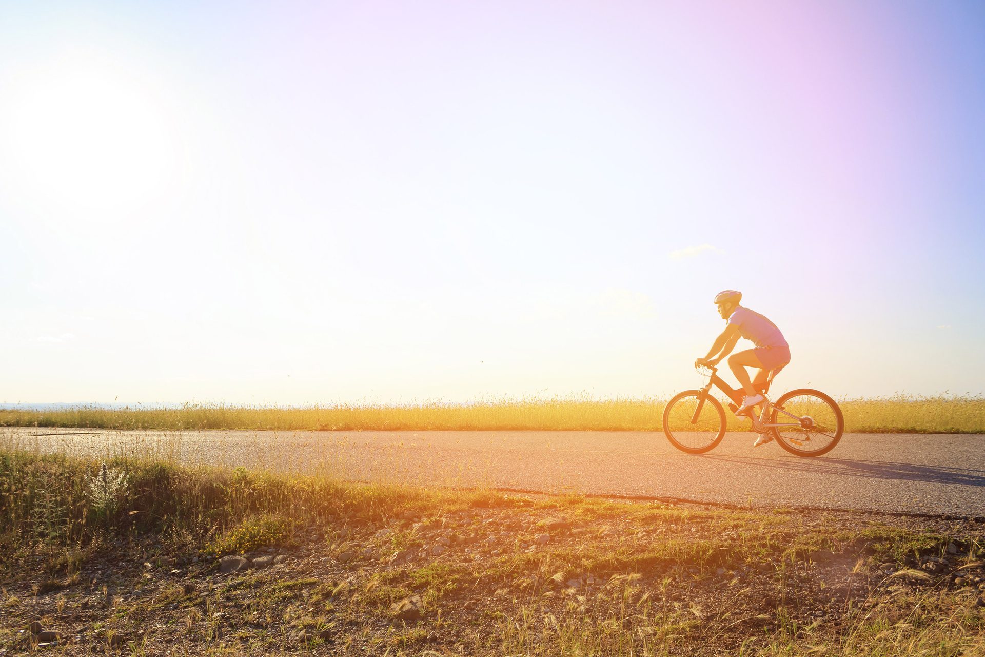 Silhouetted person cycling on a road with bright sun and warm light.