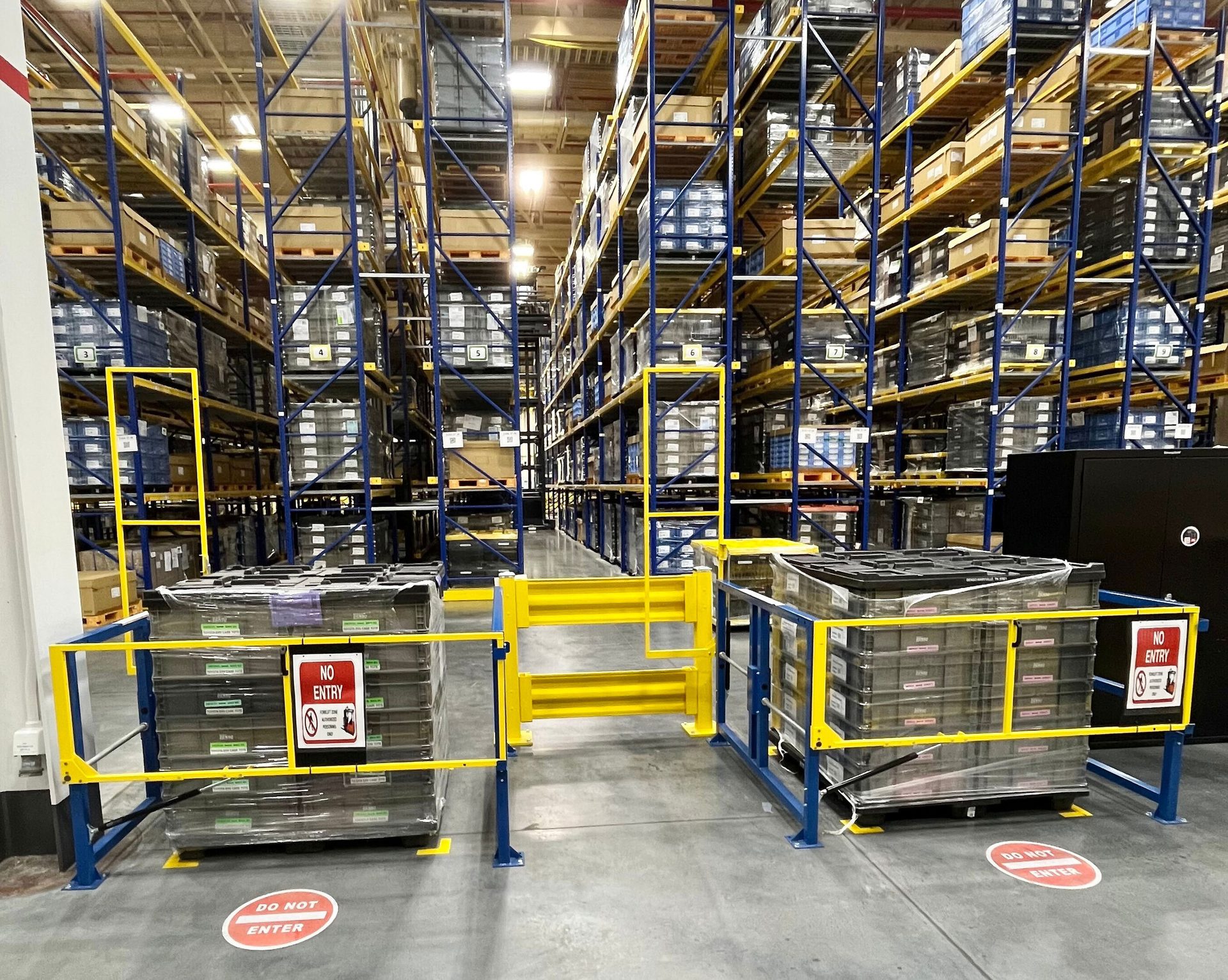 Warehouse with tall storage racks, a yellow and blue safety barrier, and "NO ENTRY" signs.