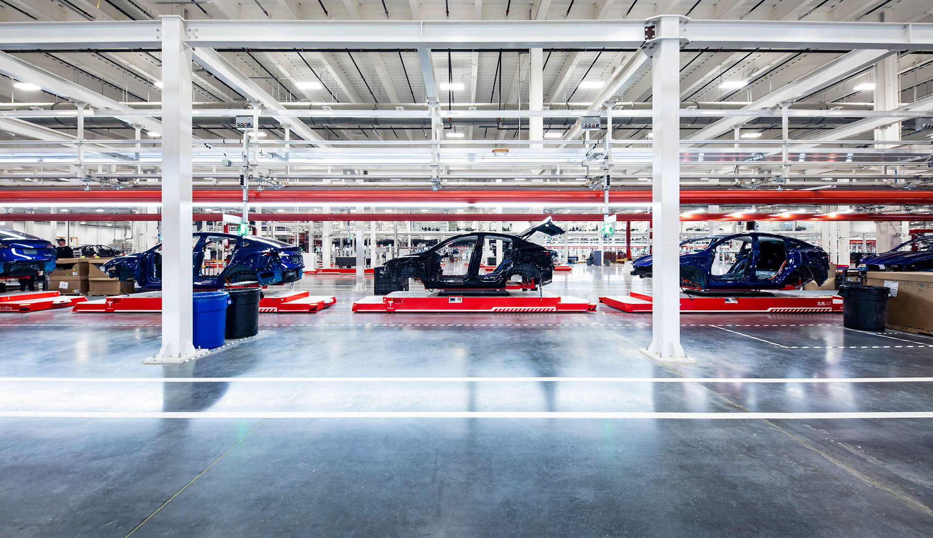 An assembly line in a factory with several car bodies on red platforms, showcasing the manufacturing process.
