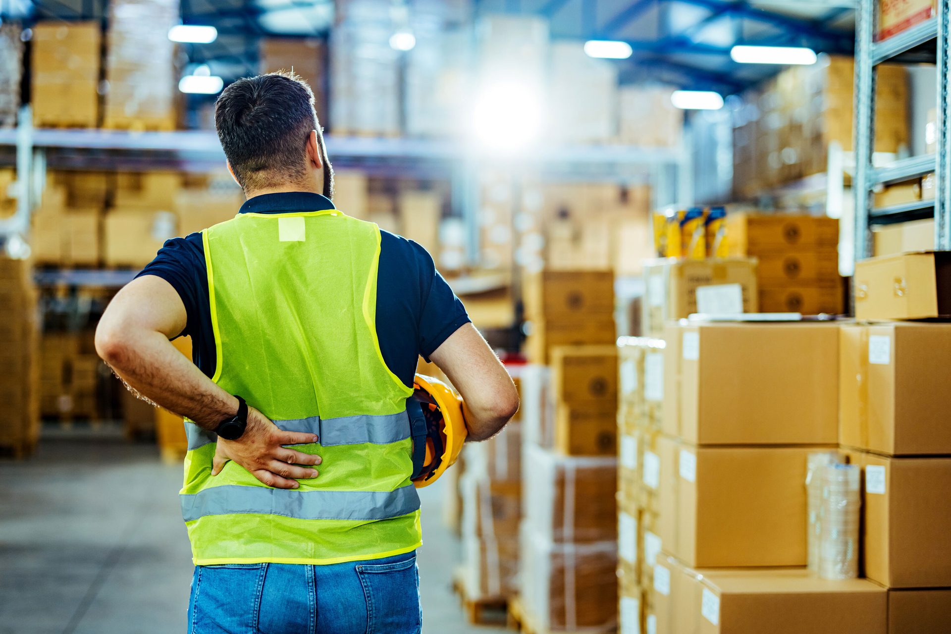 Warehouse worker with back pain, wearing safety vest.