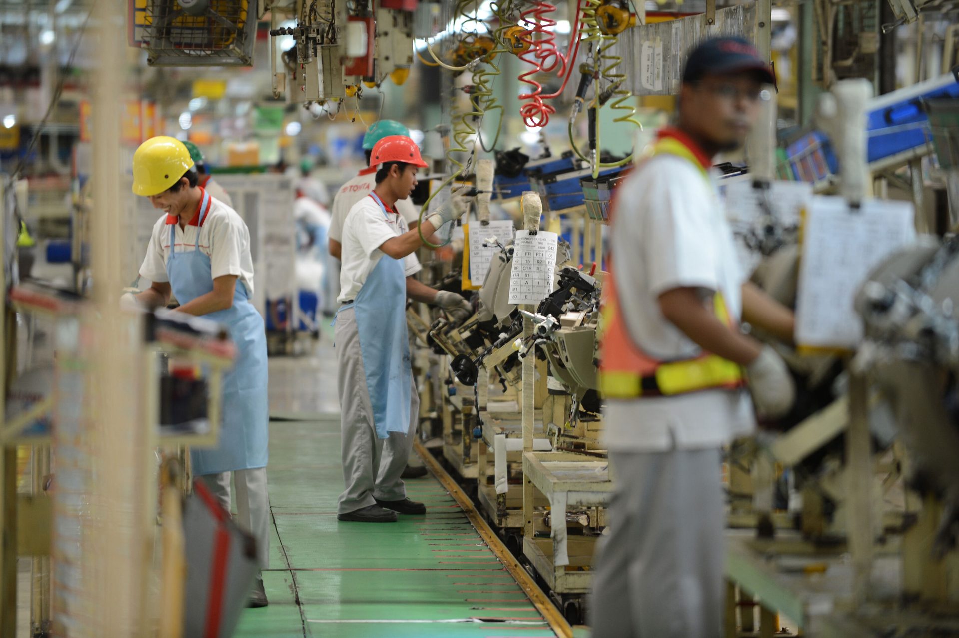 Workers on a factory assembly line, wearing safety helmets and aprons.