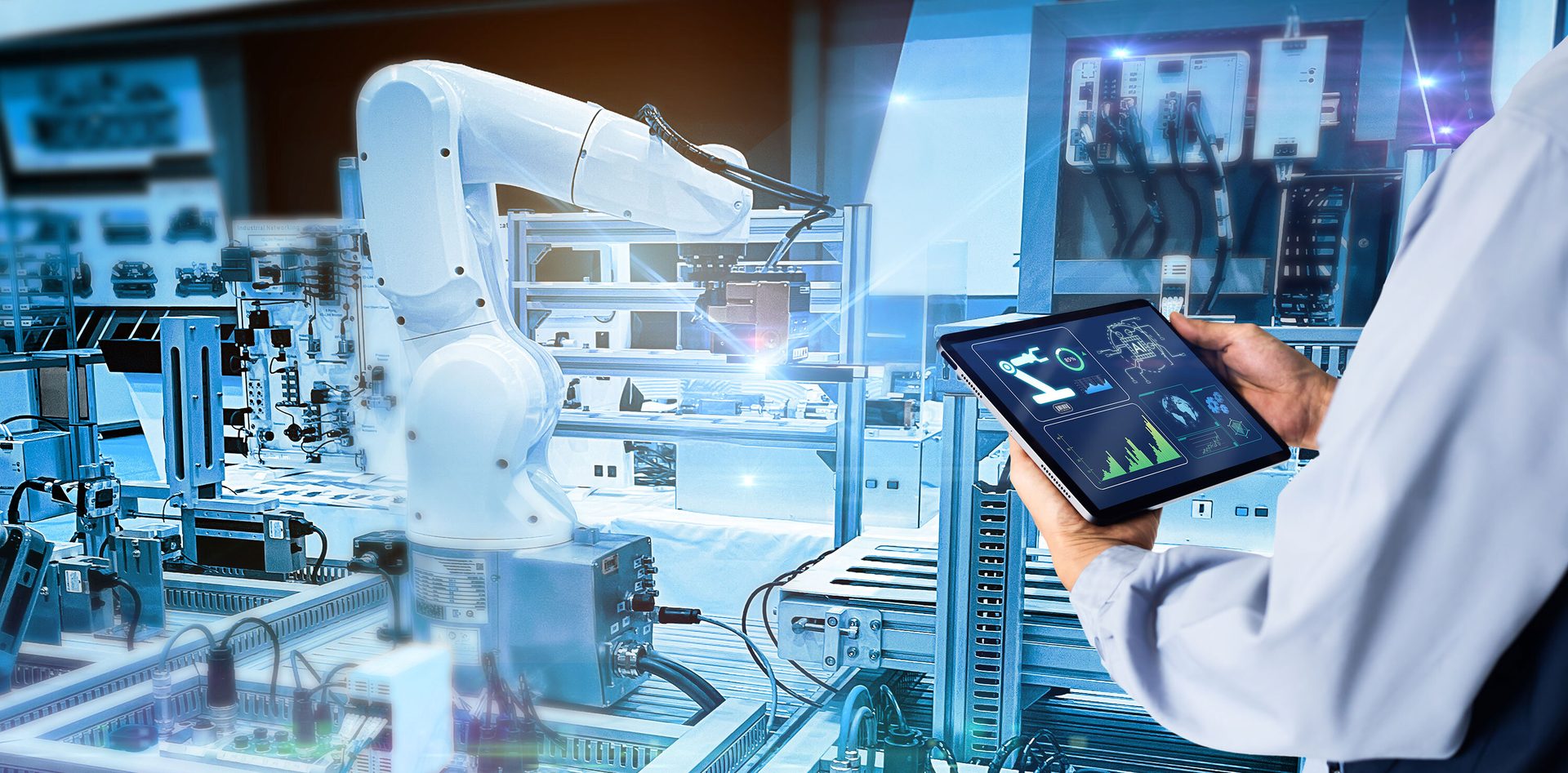 A person uses a tablet to control a robotic arm in an advanced industrial automation setting.