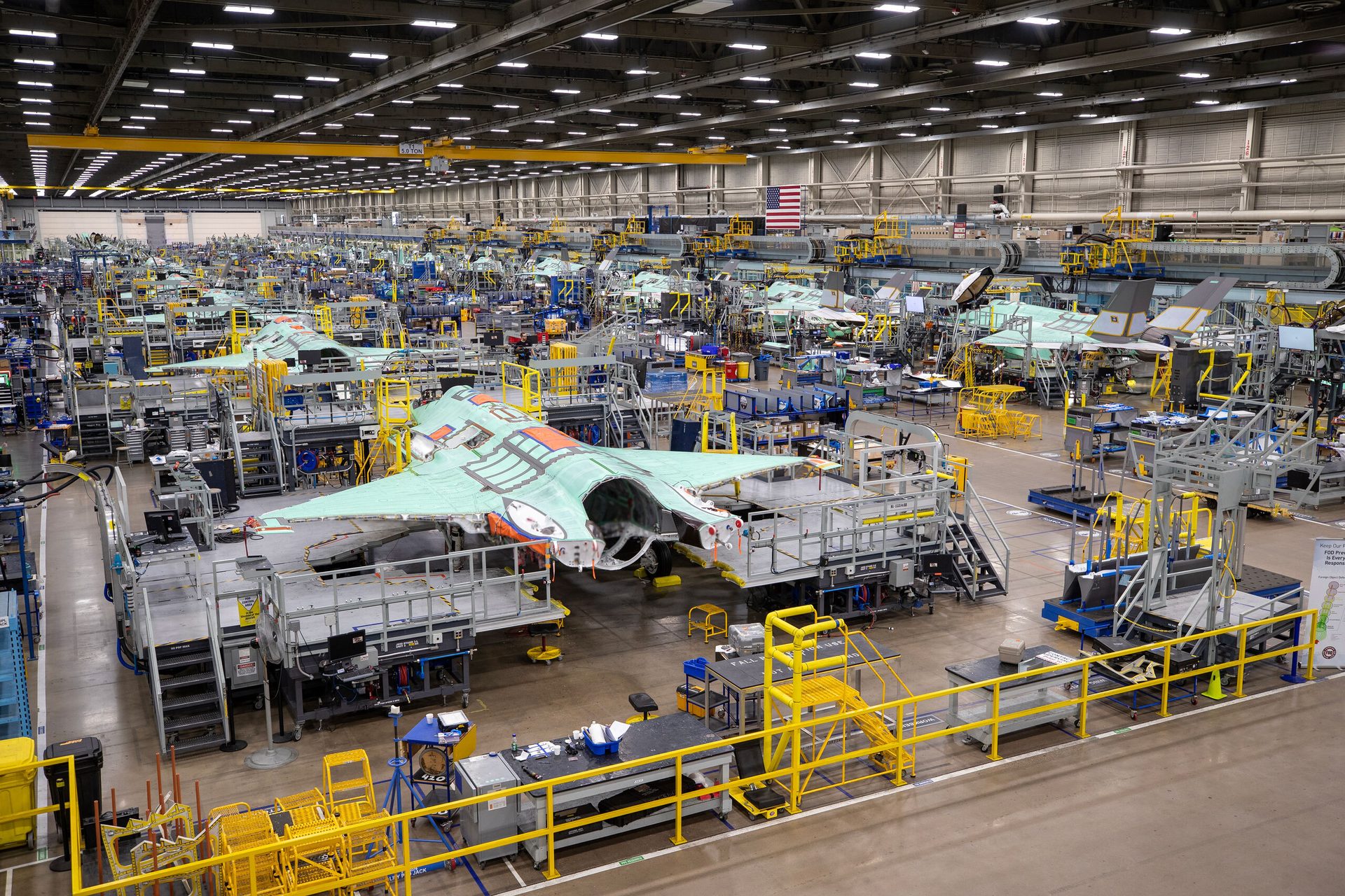 Assembly line of F-35 fighter jets in a large, busy manufacturing plant.