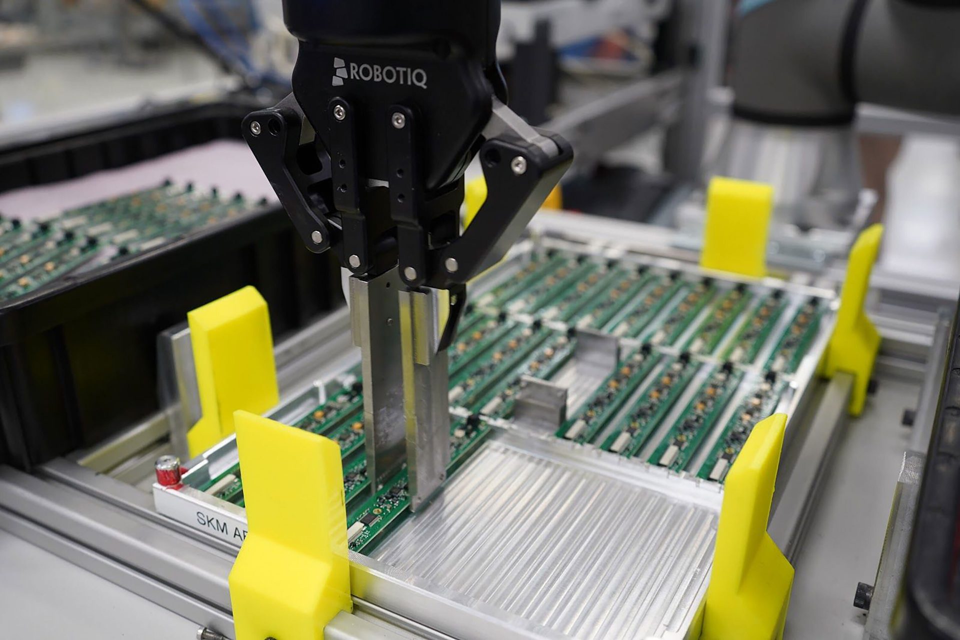Robotiq robotic arm gripping a circuit board in an assembly line.