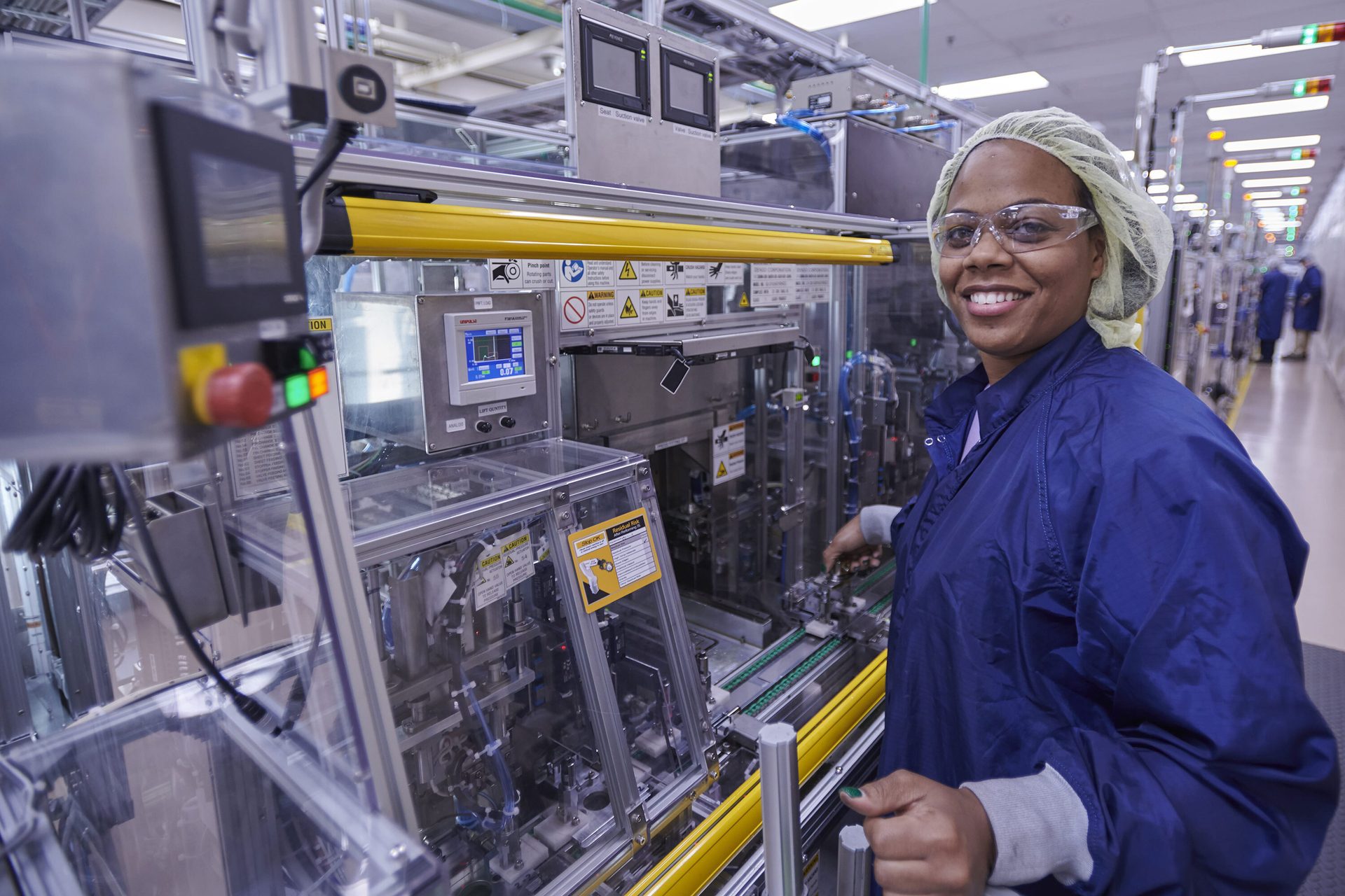 Smiling factory worker in safety gear next to manufacturing machinery.