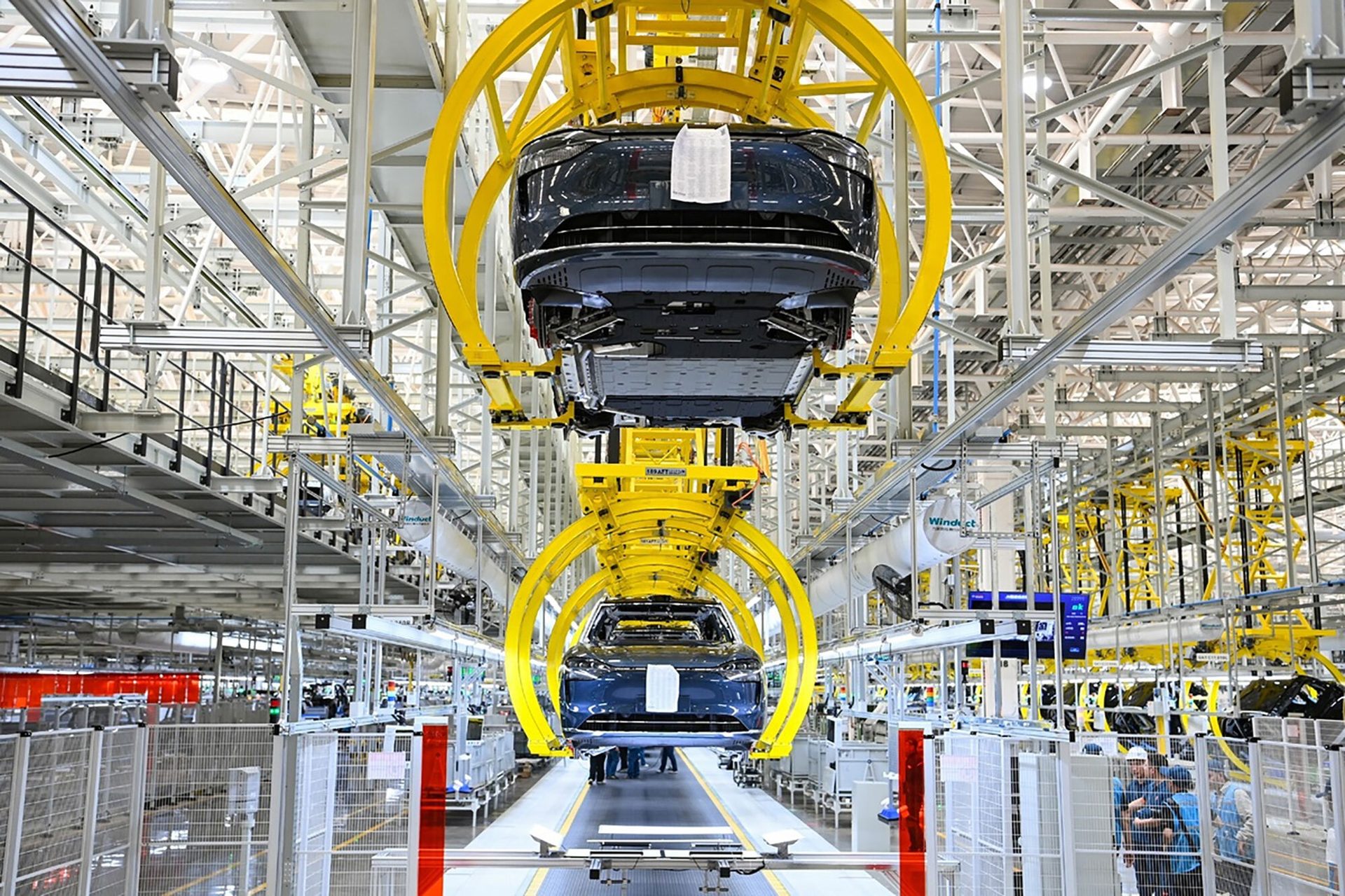 Two electric cars on yellow overhead conveyors in a factory assembly line.