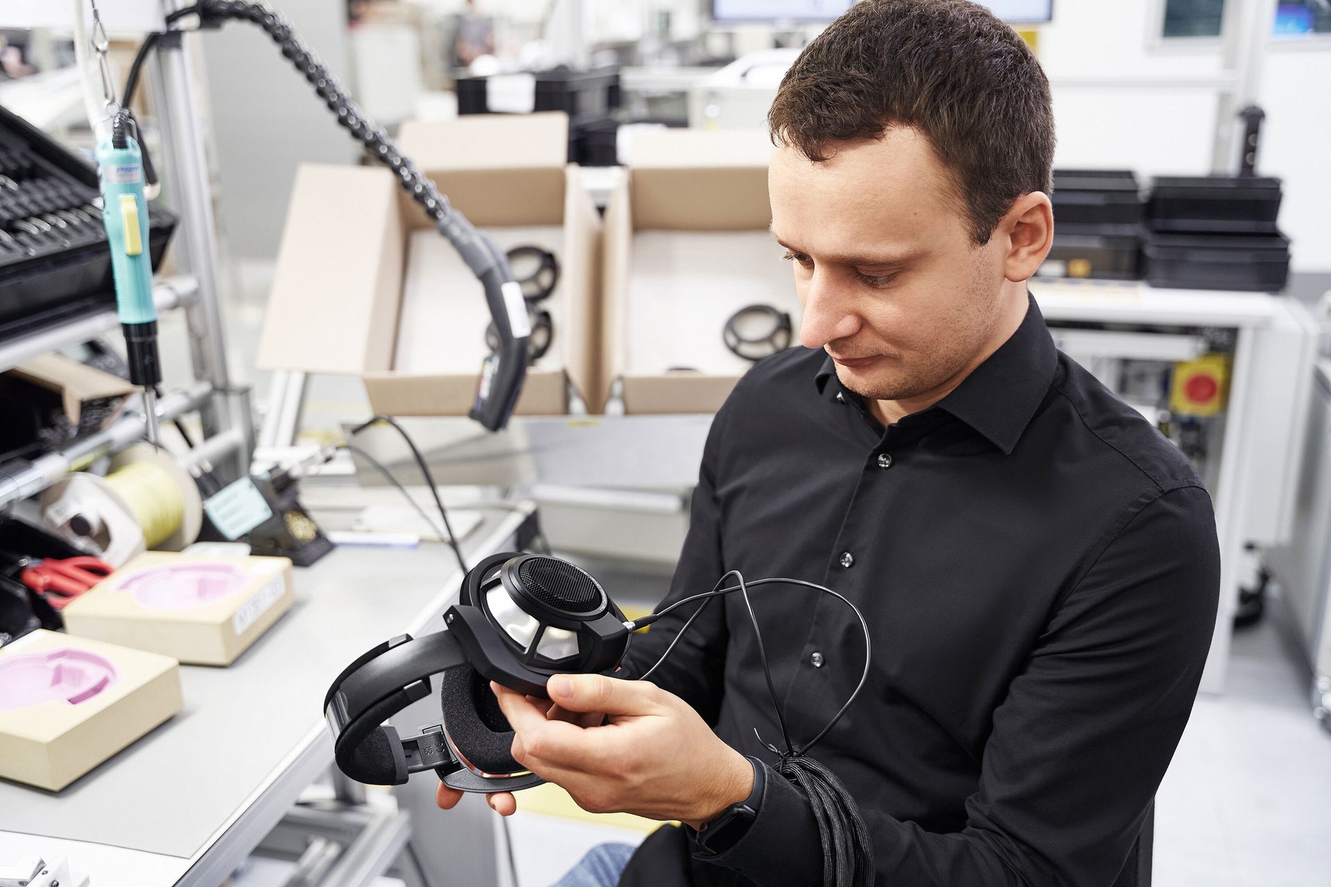 Man inspecting black headphones in an assembly environment.