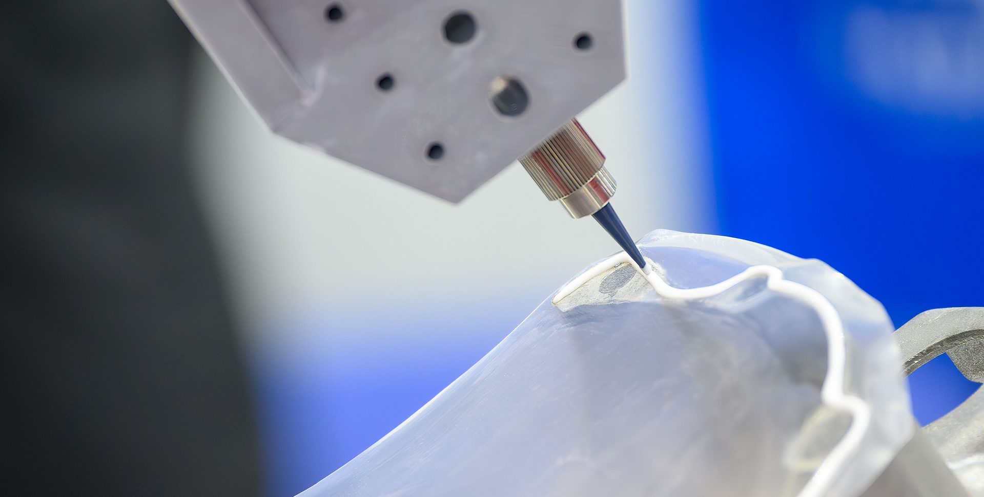 Robotic arm precisely dispensing white sealant or adhesive onto a translucent object.