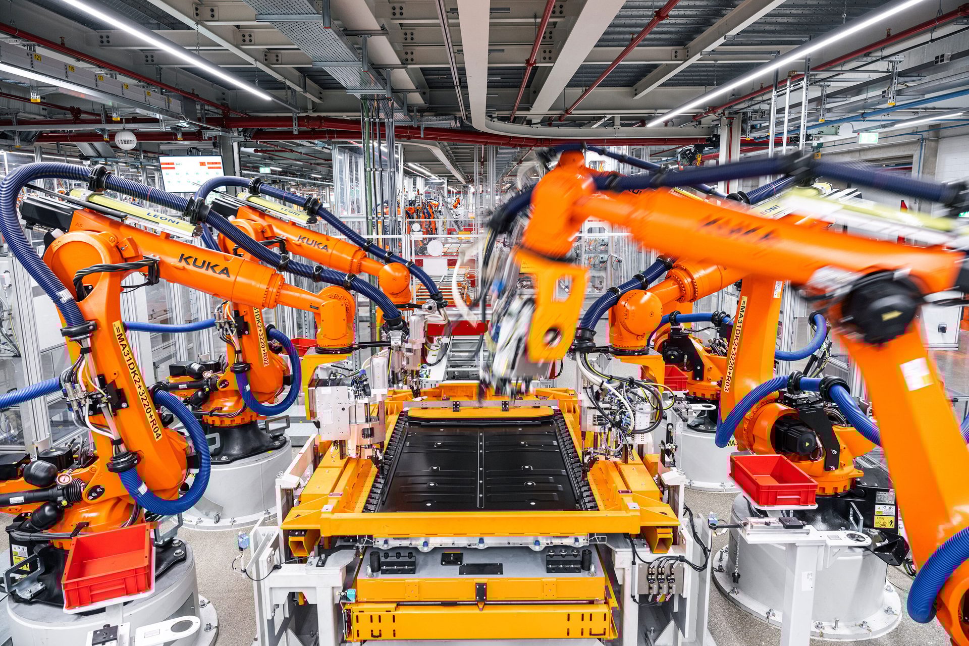 Orange KUKA industrial robots on an assembly line, manufacturing a large component.