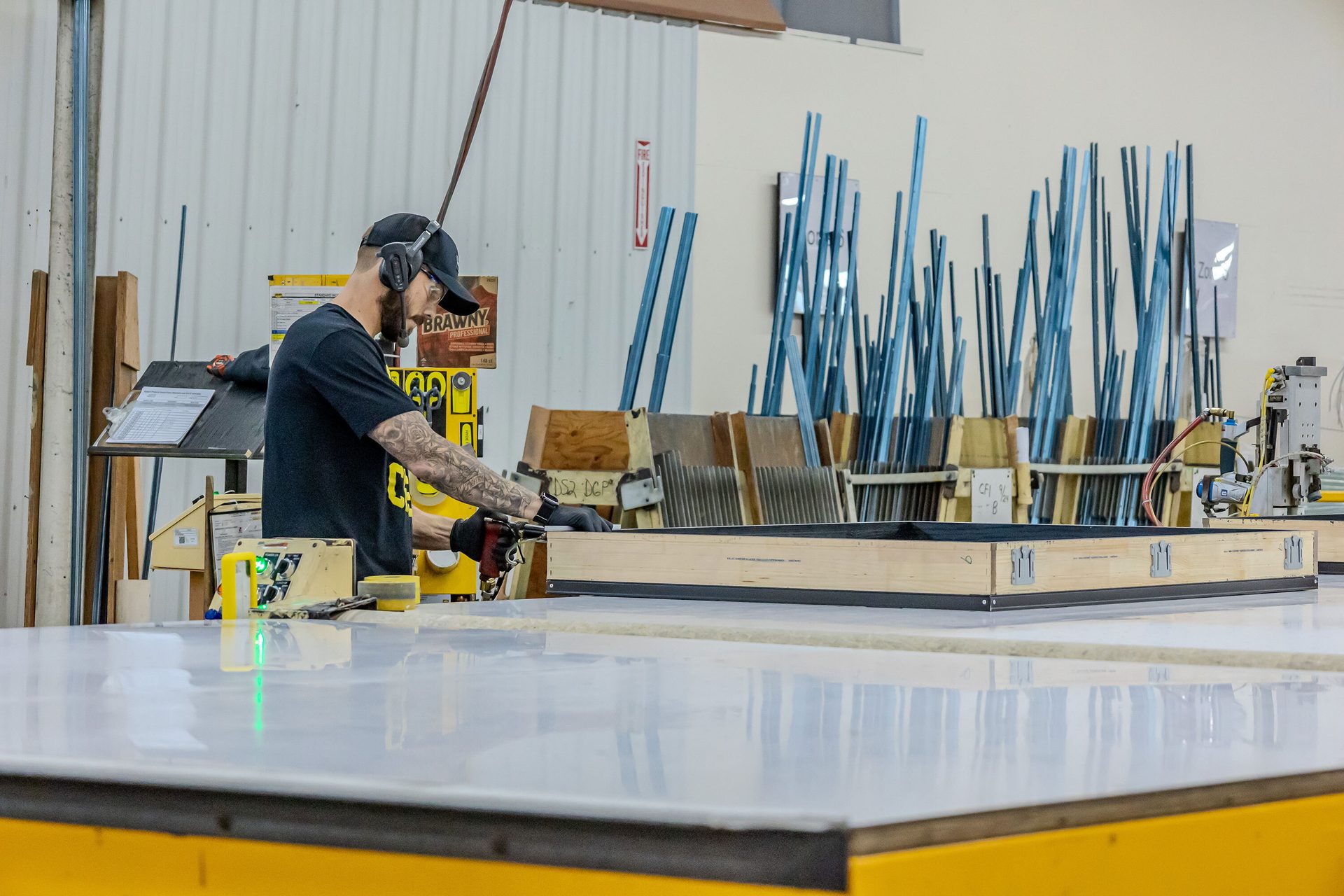 A worker in a workshop assembling a wooden frame, wearing ear protection and gloves.
