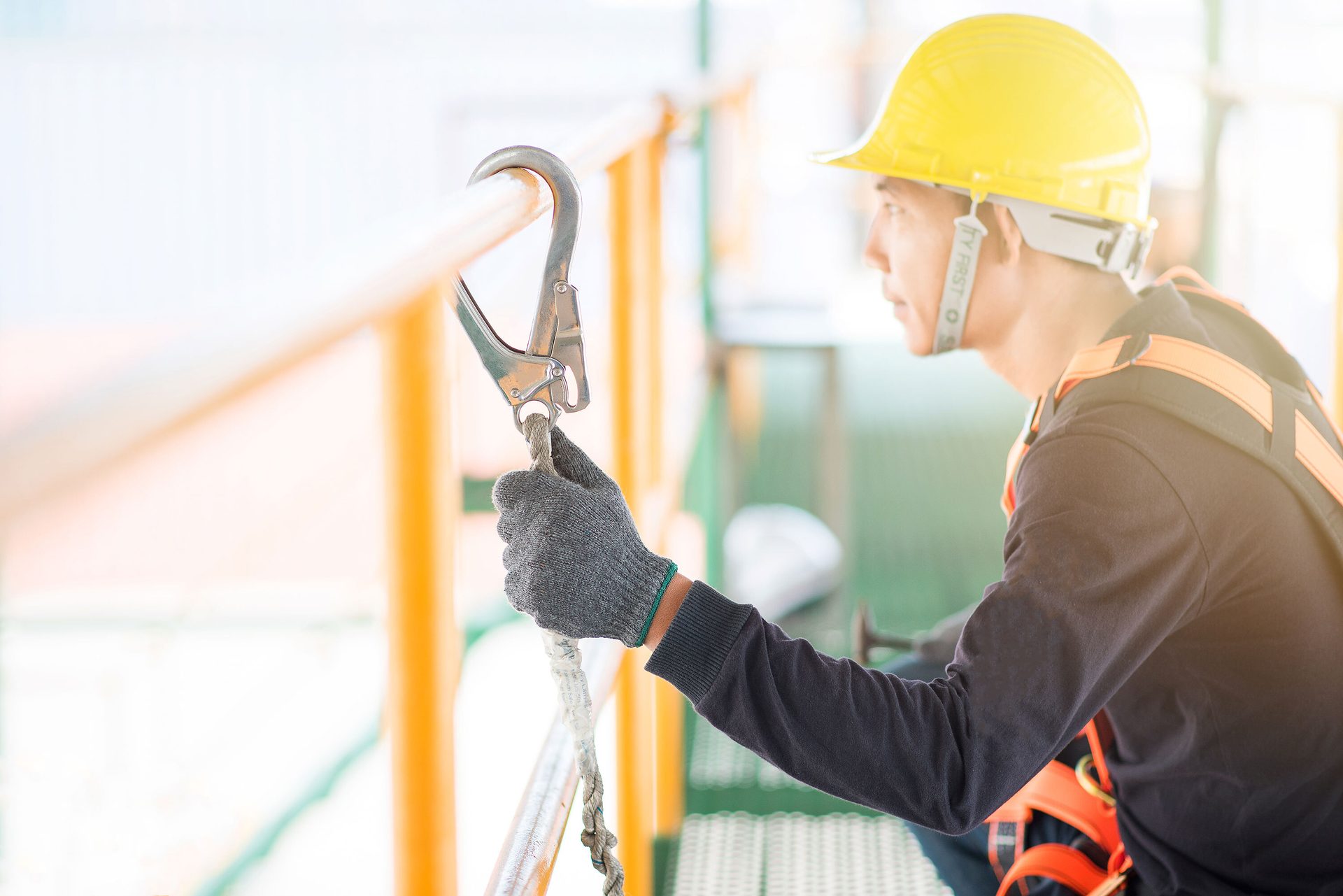 Worker in hard hat and harness attaches safety hook to a railing.