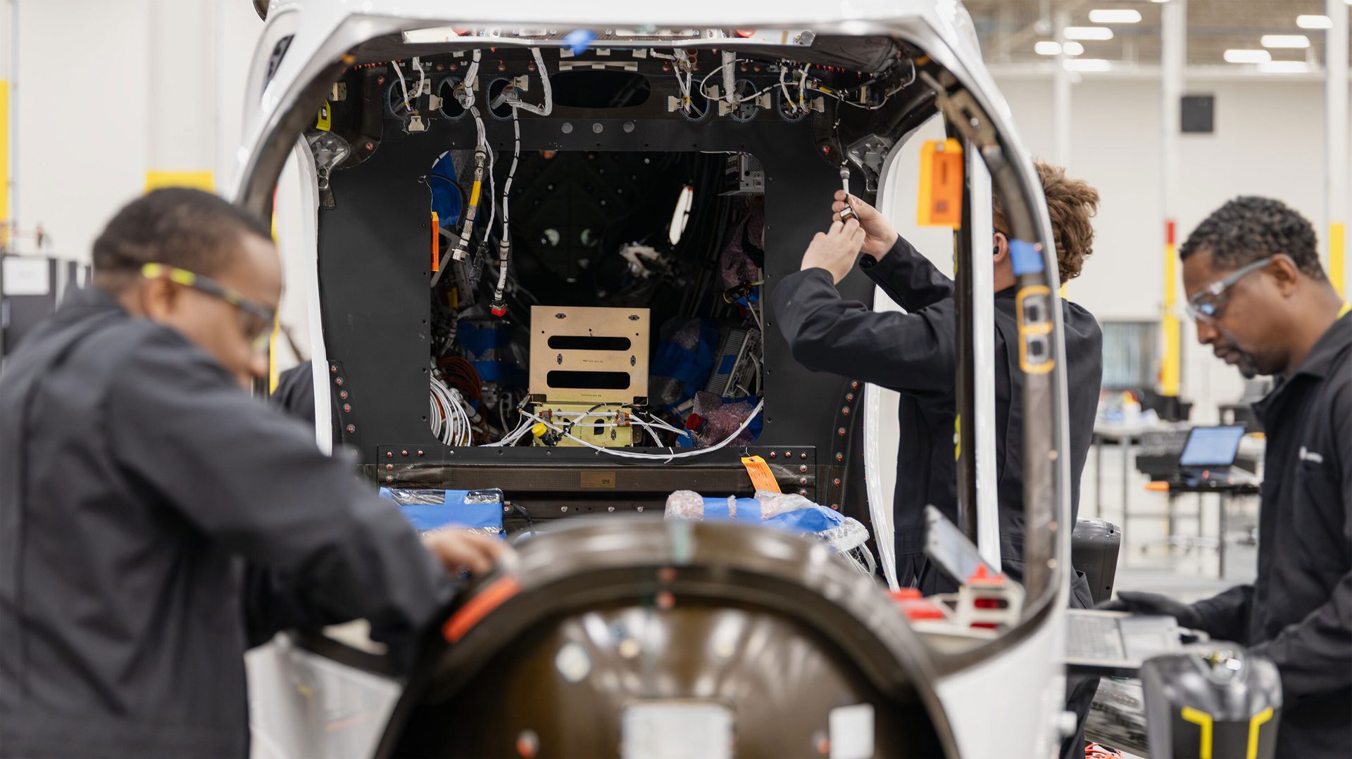 Technicians assembling complex wiring and components in an aerospace vehicle.