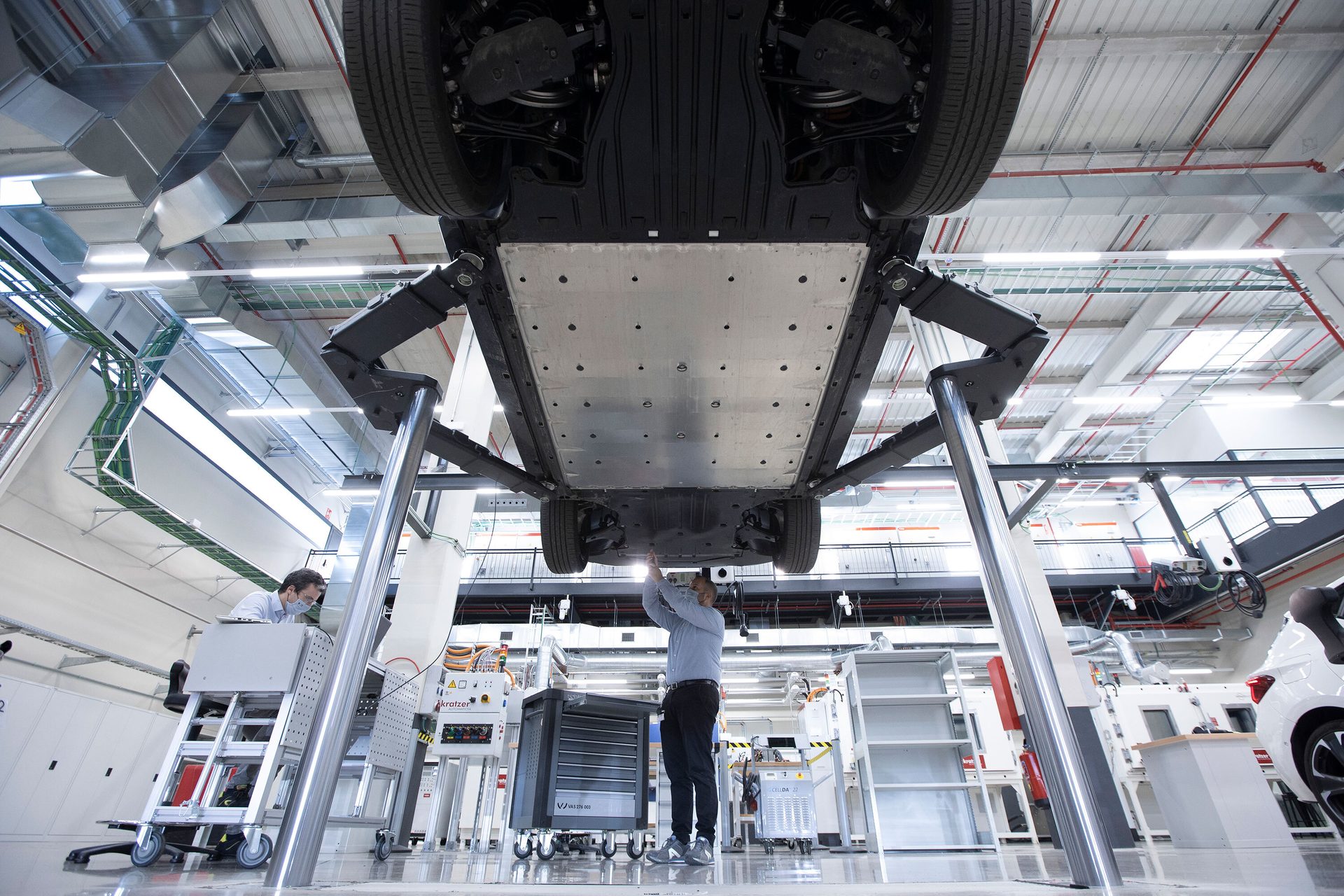 Worker inspects the battery pack of an electric car elevated on a workshop lift.