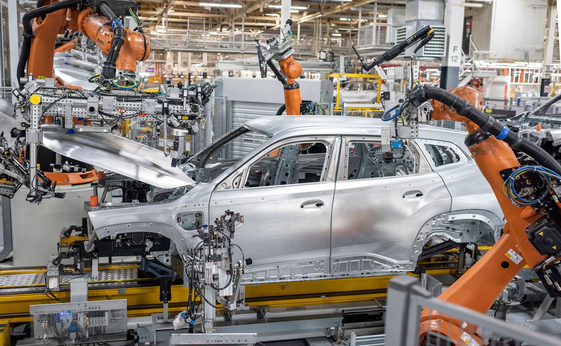 Robotic arms assemble a silver car body on an automated factory line.