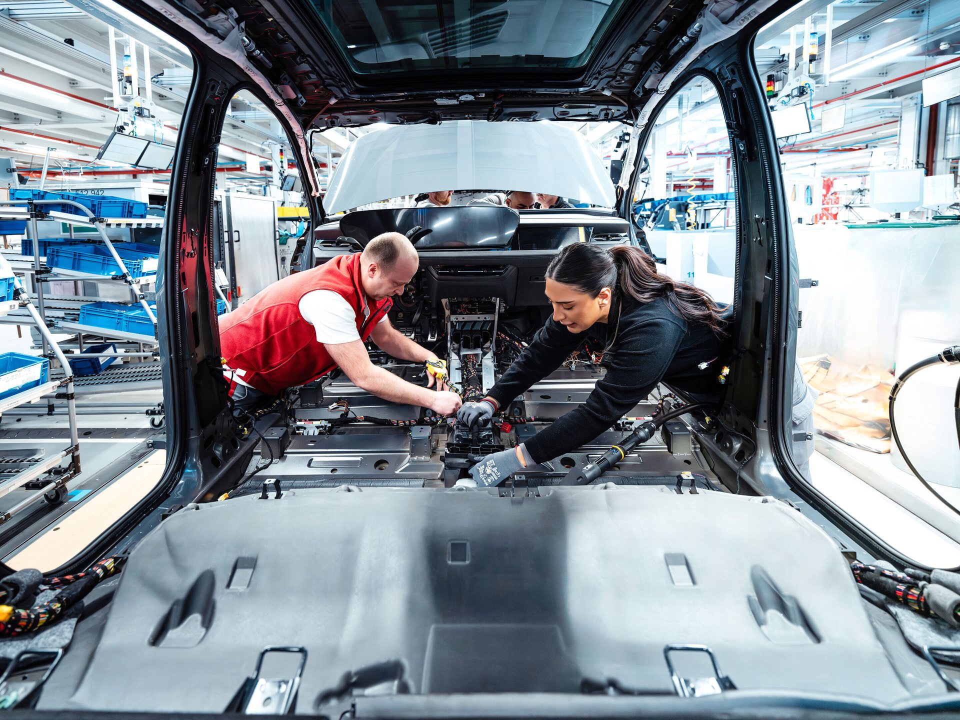 Two workers install components inside a car body on an assembly line.