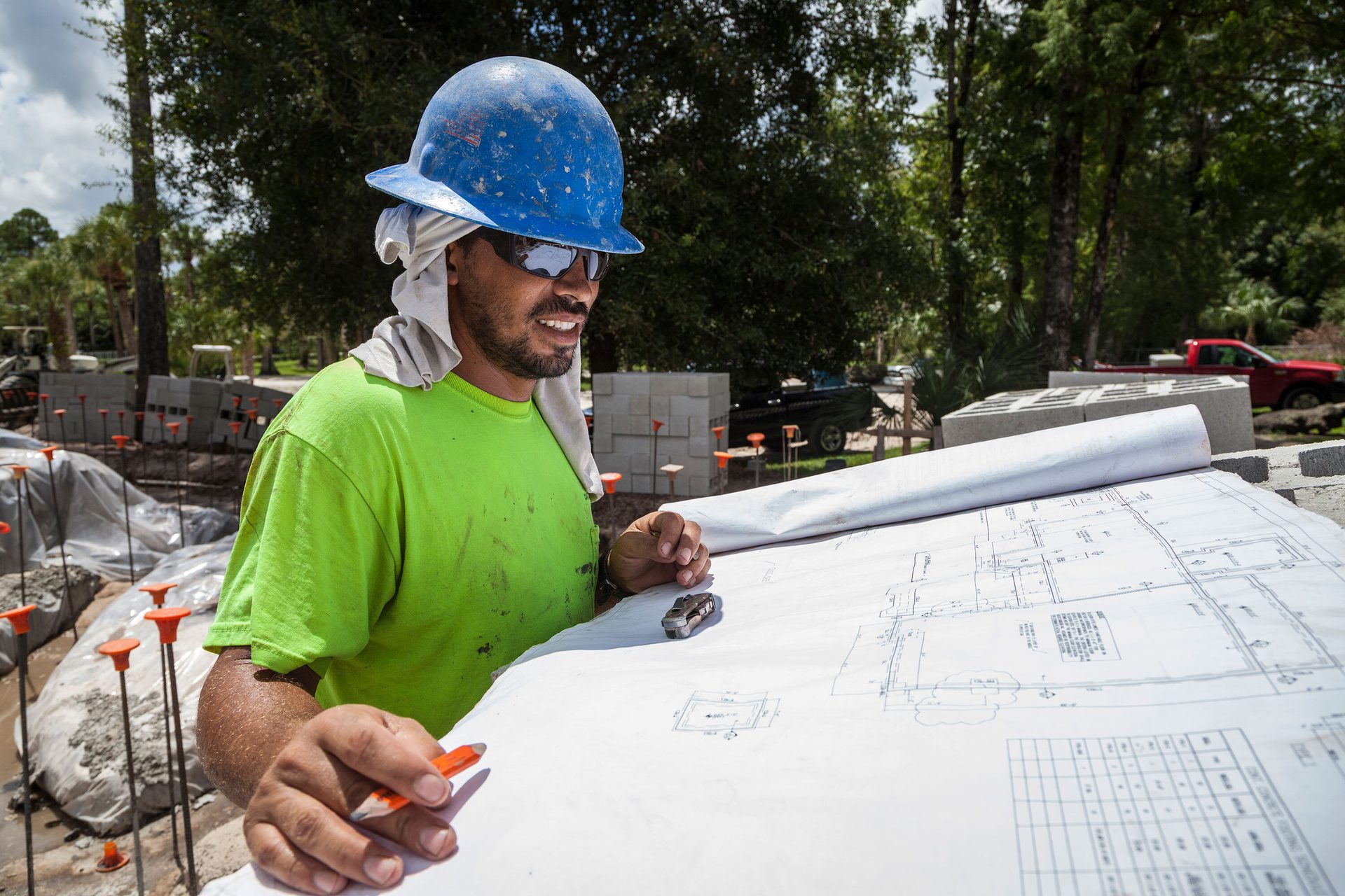 Construction worker in hard hat and sunglasses reviews blueprints at a job site.