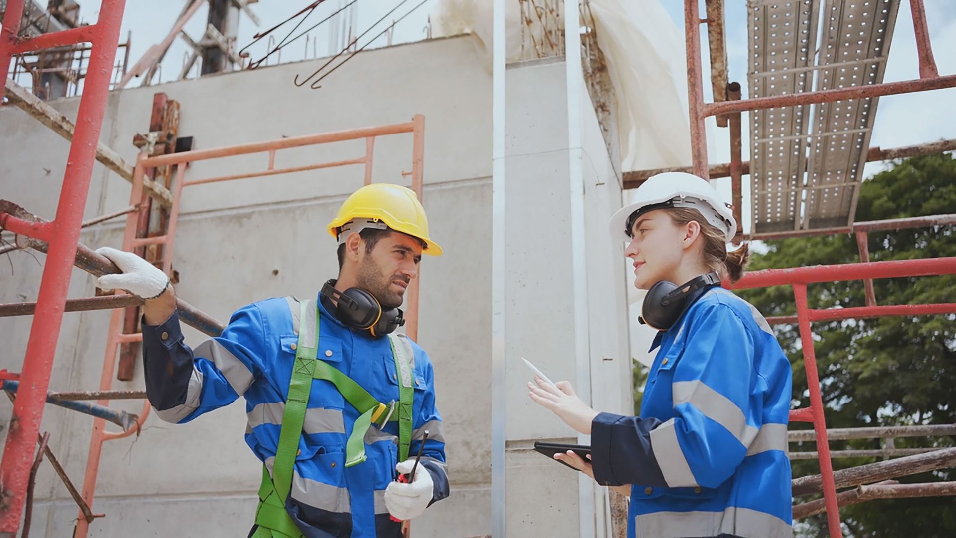 Two construction workers in safety gear discuss on a building site.