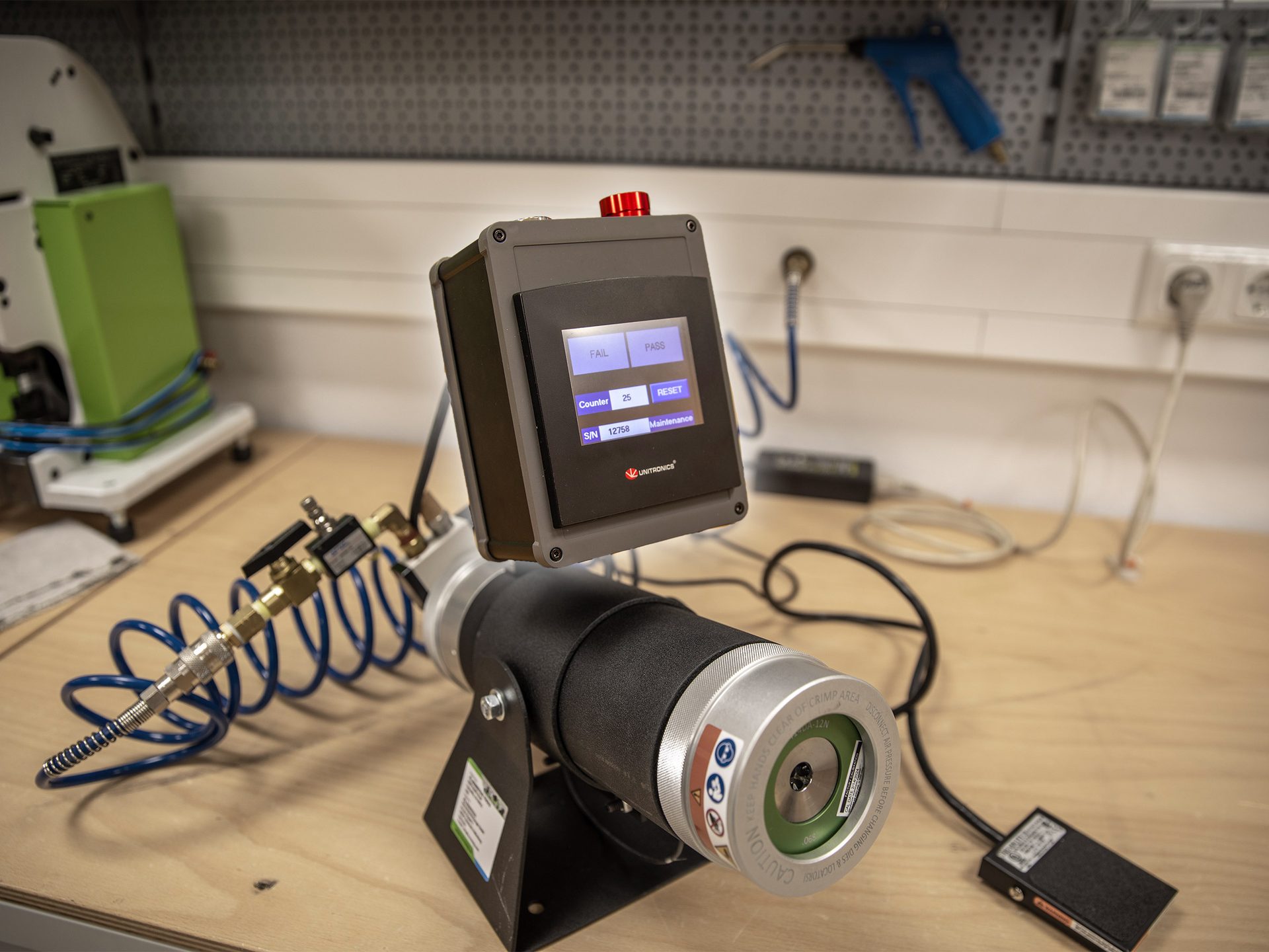 Workbench with a Unitronics controller, pneumatic crimping tool, air hose, and foot pedal.