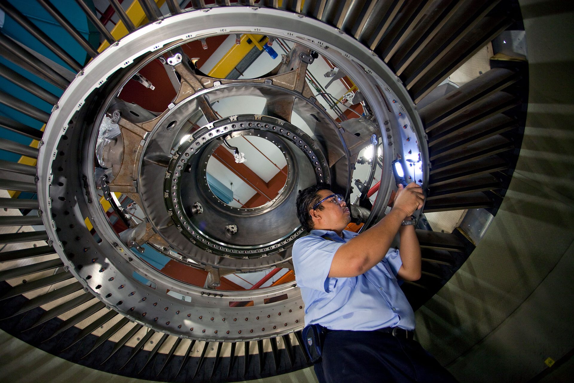 Technician inspecting a large jet engine with a flashlight.