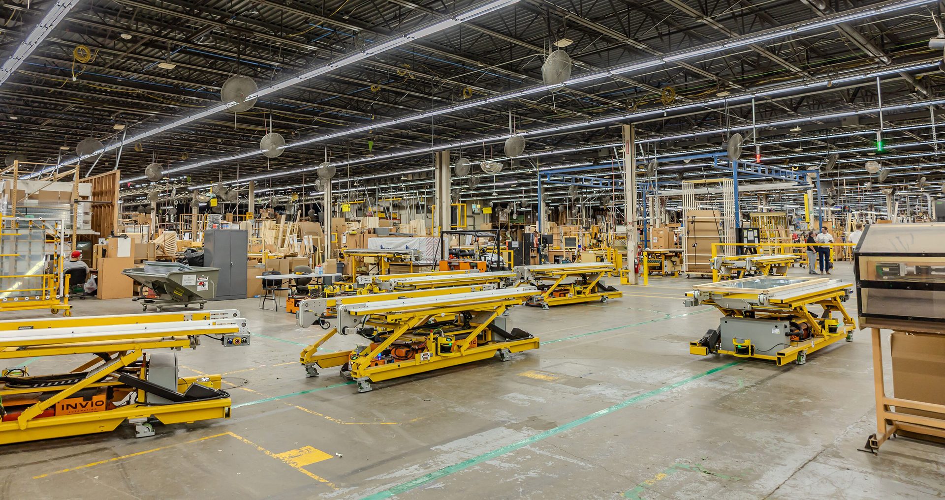 Busy factory floor with yellow robotic platforms, industrial equipment, and workers.