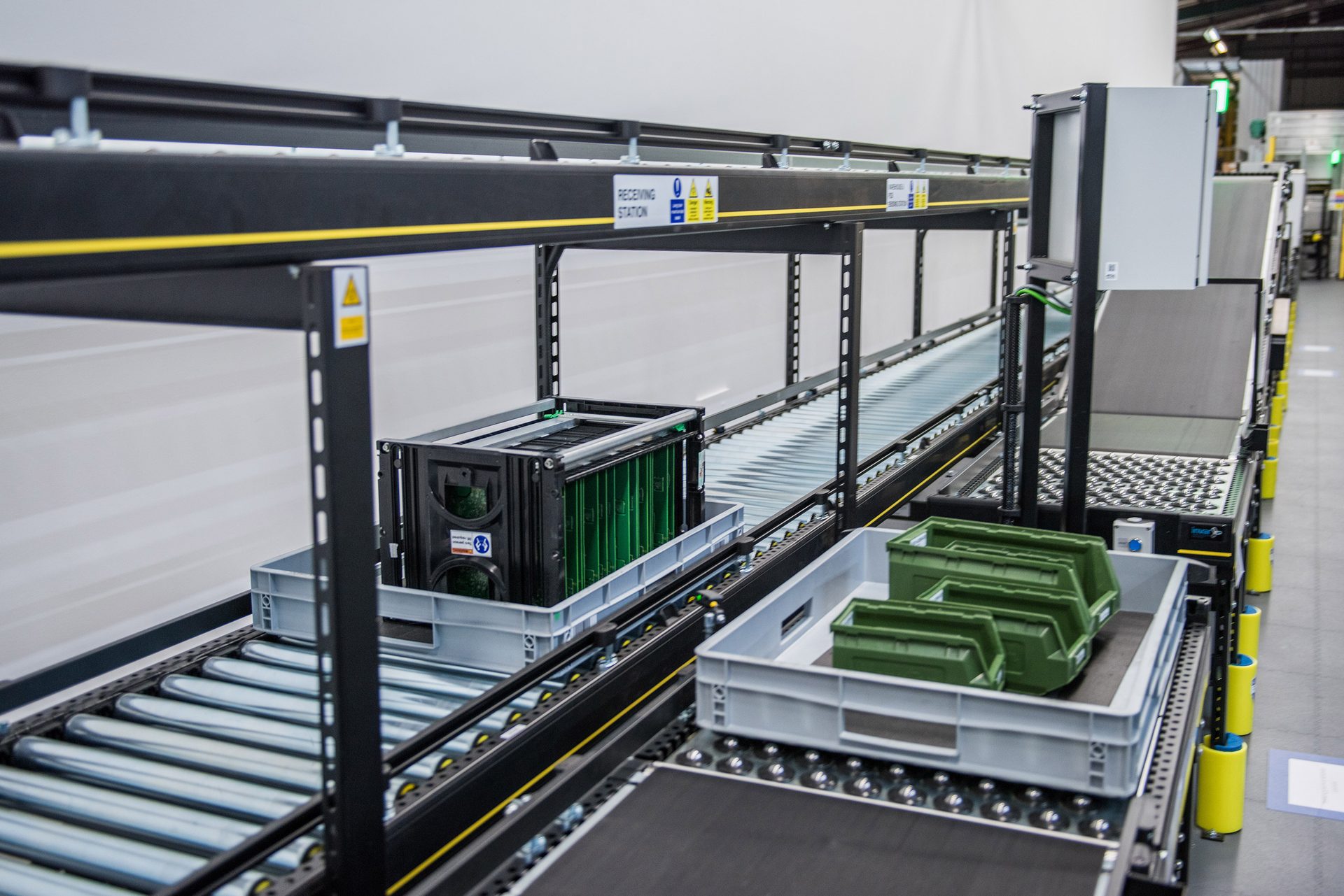 Industrial conveyor system with gray crates and green bins.