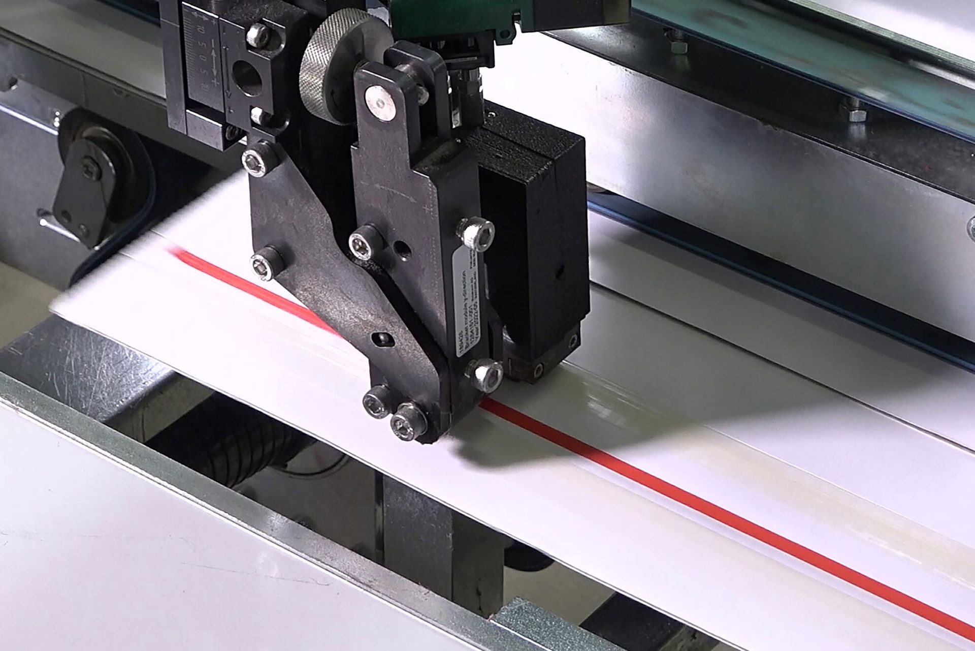 Close-up of an industrial machine precisely cutting or processing white material with a distinct red line.