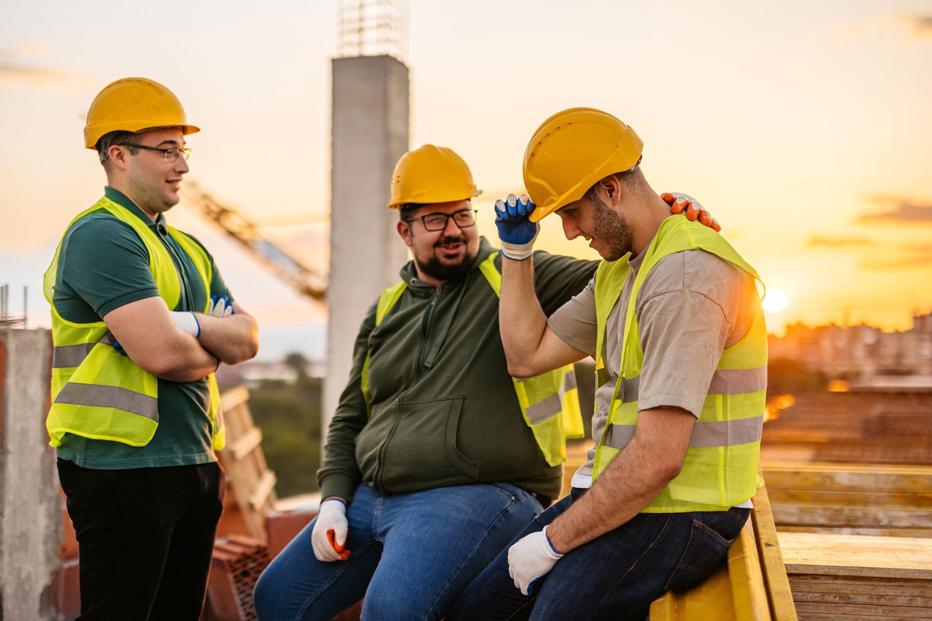 Three construction workers in safety gear on a construction site at sunset.