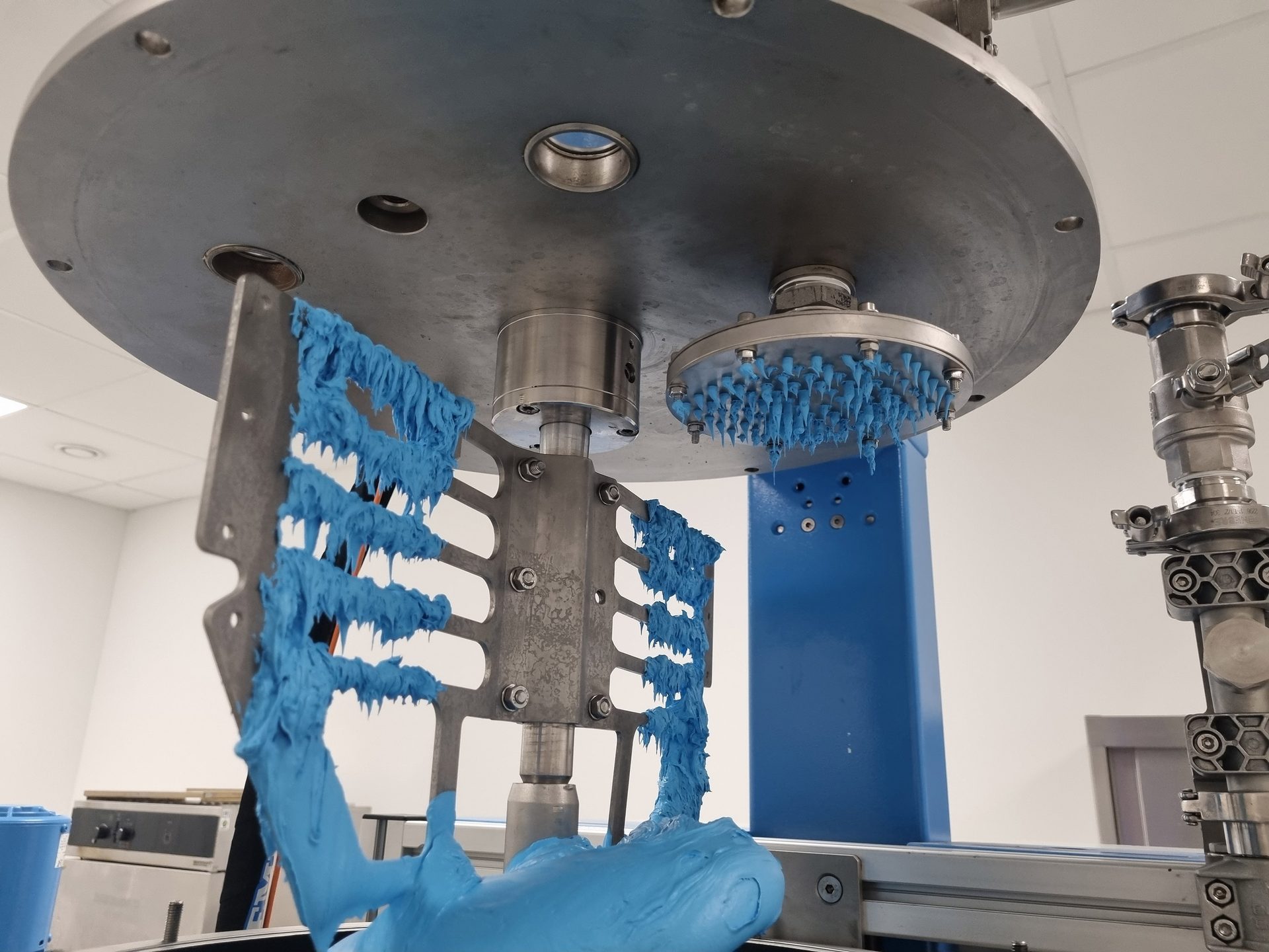 Industrial mixer with blue, viscous material on a large stirrer and a spiky disc.