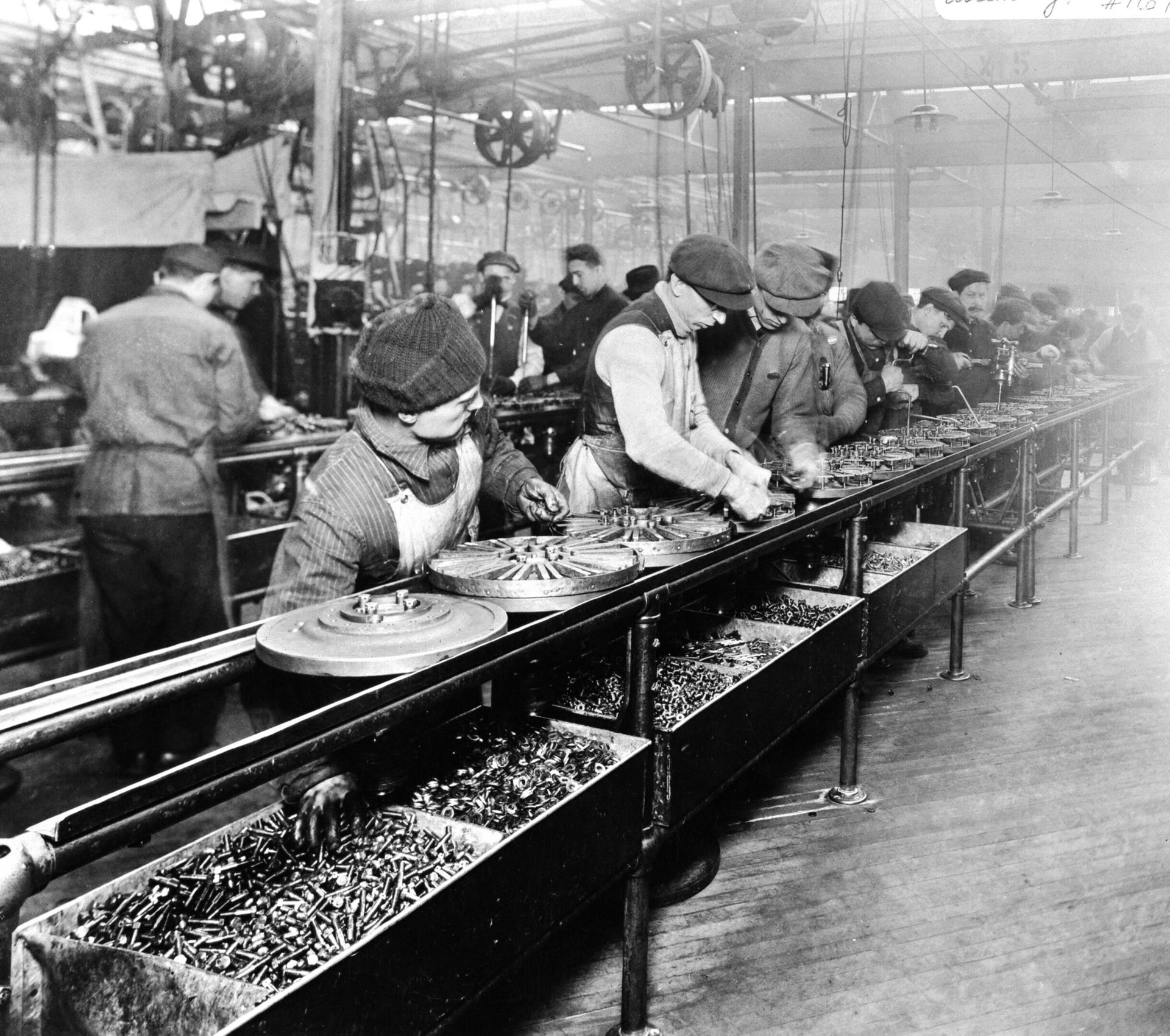 Workers on an assembly line handling small parts, with bins of components.