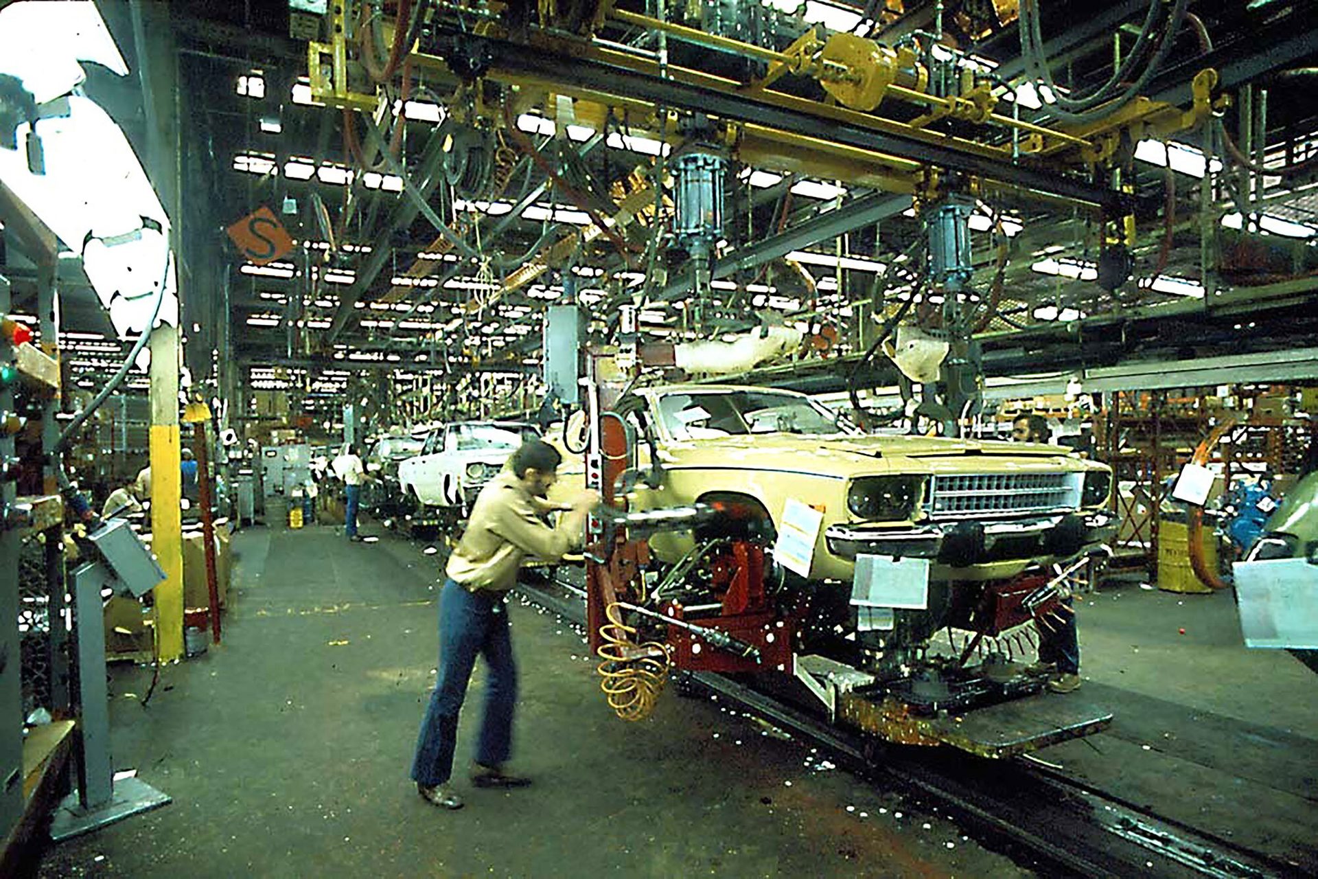 Worker assembling a yellow car on an assembly line.