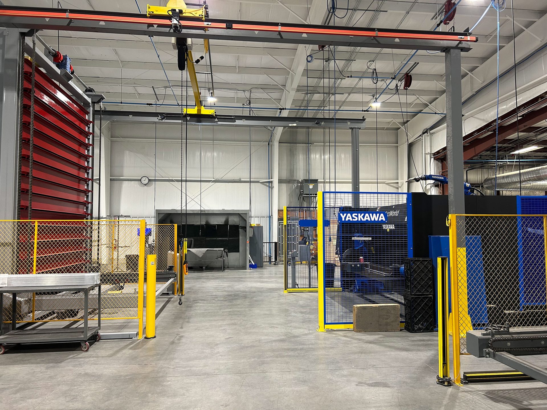 Factory floor with overhead crane, red automated storage, and Yaskawa robots.