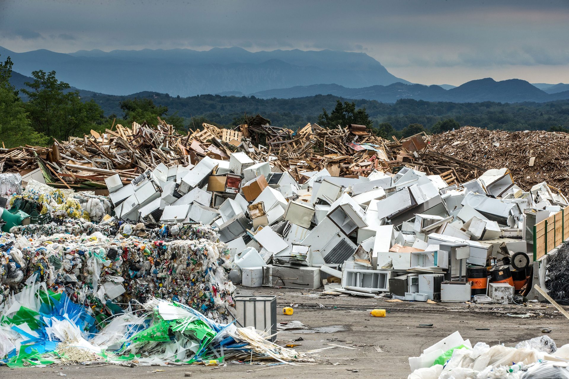 Large outdoor piles of white appliances, baled plastics, and wood waste at a recycling center.