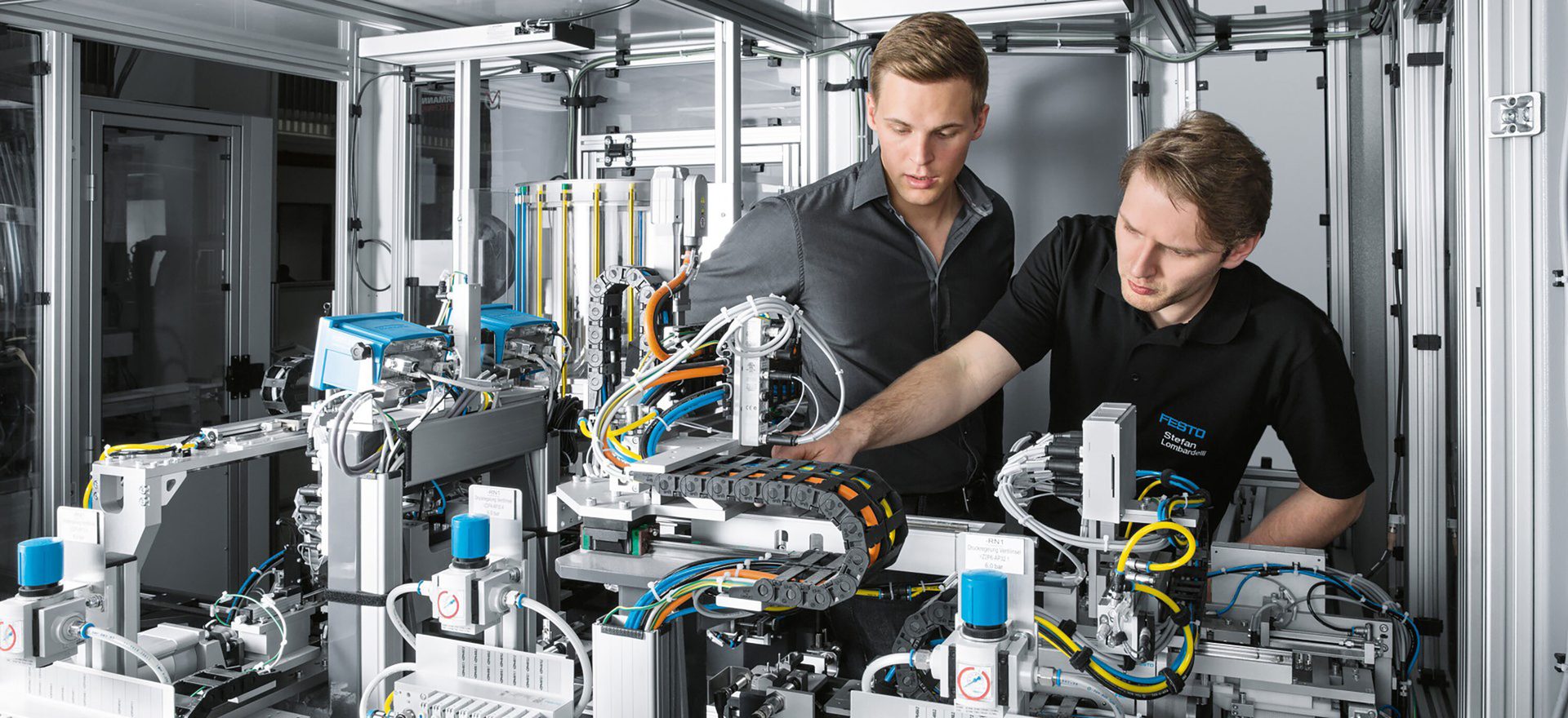 Two men work on complex industrial machinery with many wires and components.